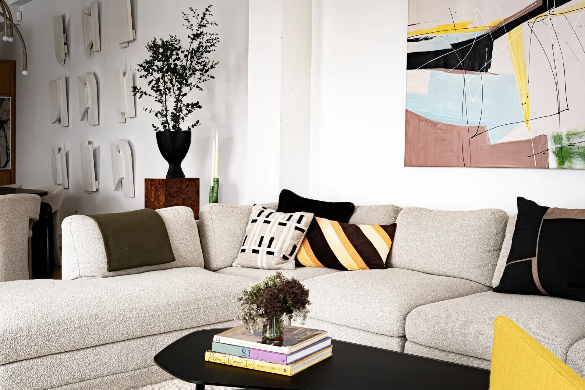 Contemporary living room with cream sectional sofa, black coffee table, geometric artwork, and yellow accent pieces, designed by Delia Kenza Interiors.