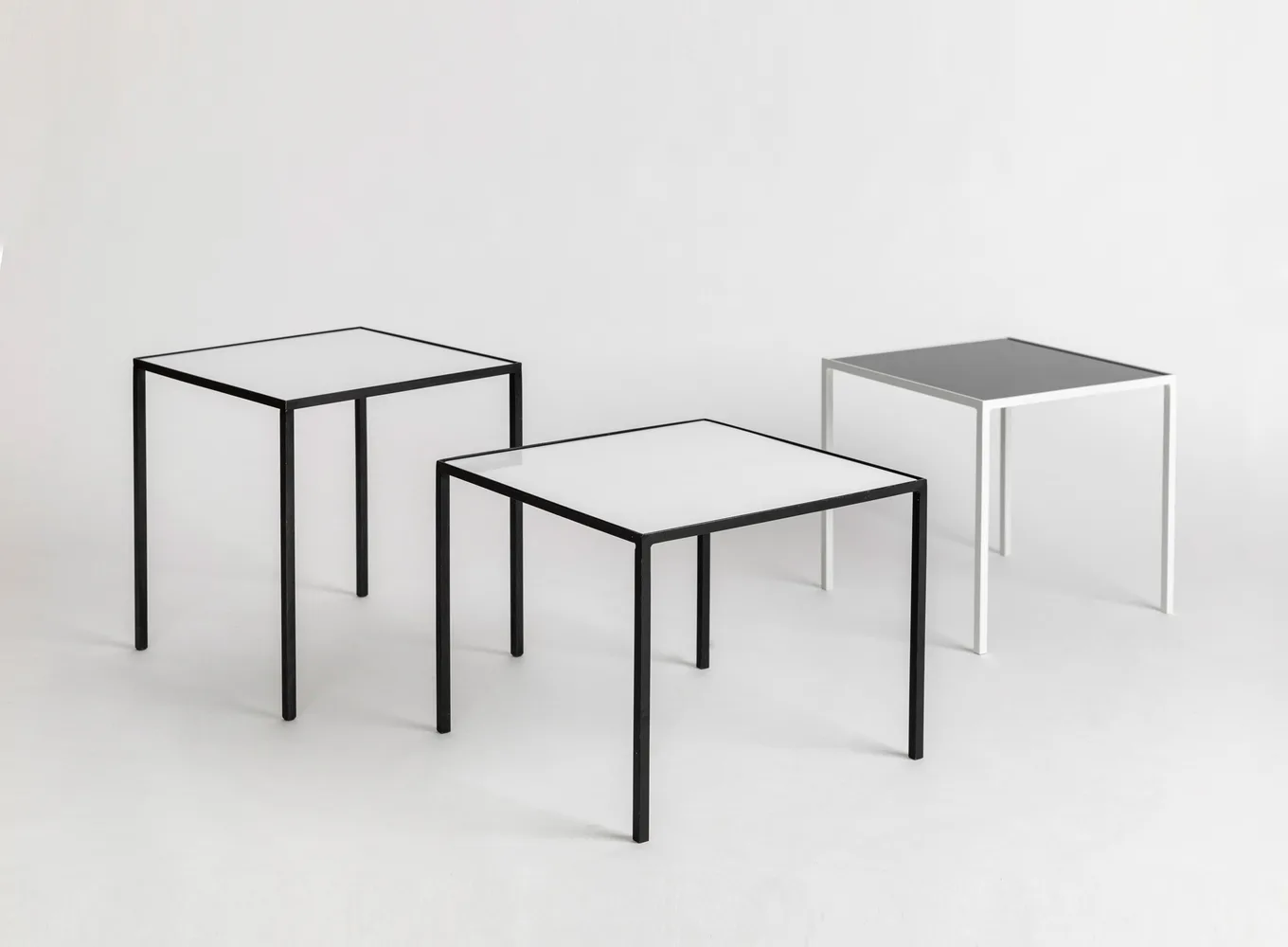 Three minimalist tables with clean lines and metal frames in varying sizes arranged on a neutral ground, showcasing furniture design by Demisch Danant.