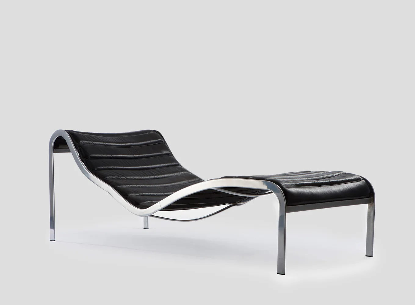Modern lounge chair with curved black leather seat and chrome frame, accompanied by matching ottoman, shown against neutral background by Demisch Danant.