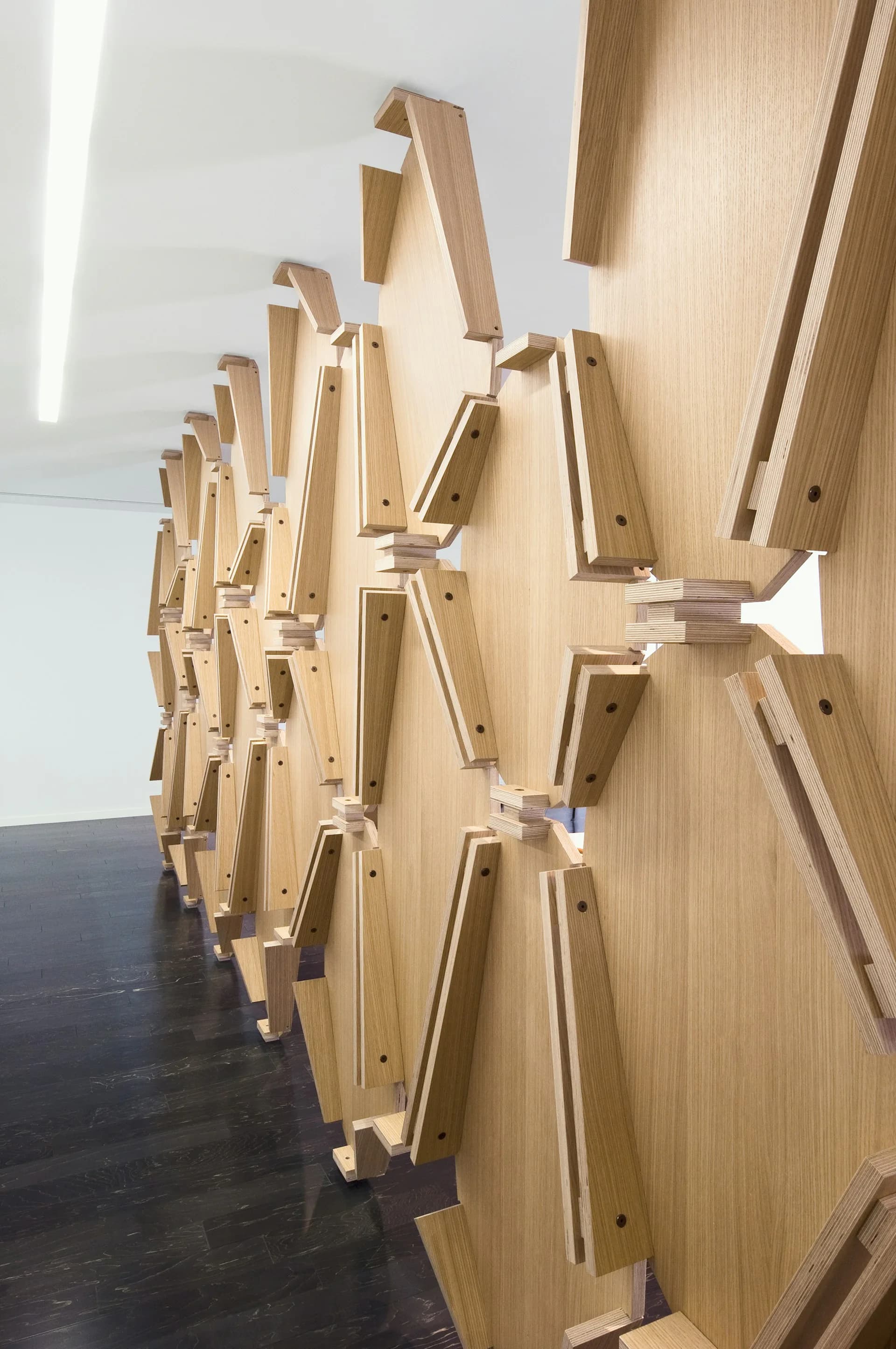 Wooden architectural installation with angled timber elements and white connectors creating a dynamic sculptural form in a gallery space by Desai Chia Architecture PC.