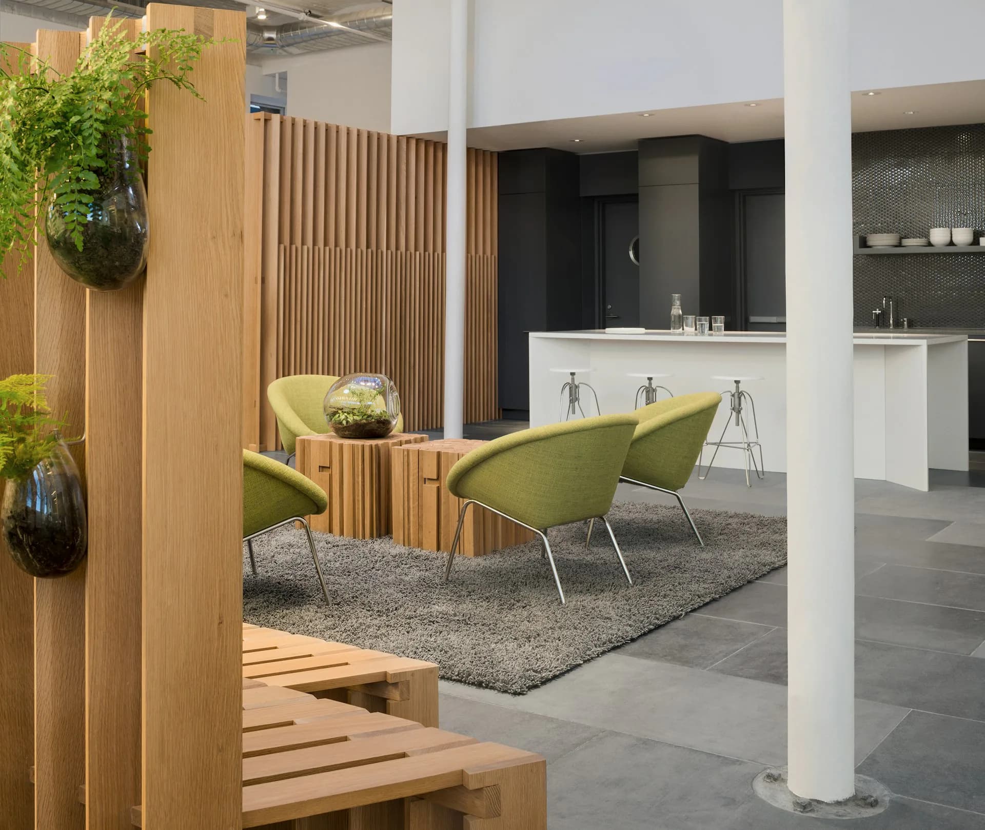 Modern showroom interior with natural wood slat partition, green upholstered seating, gray terrazzo flooring, and white kitchen display in background by Desai Chia Architecture PC.