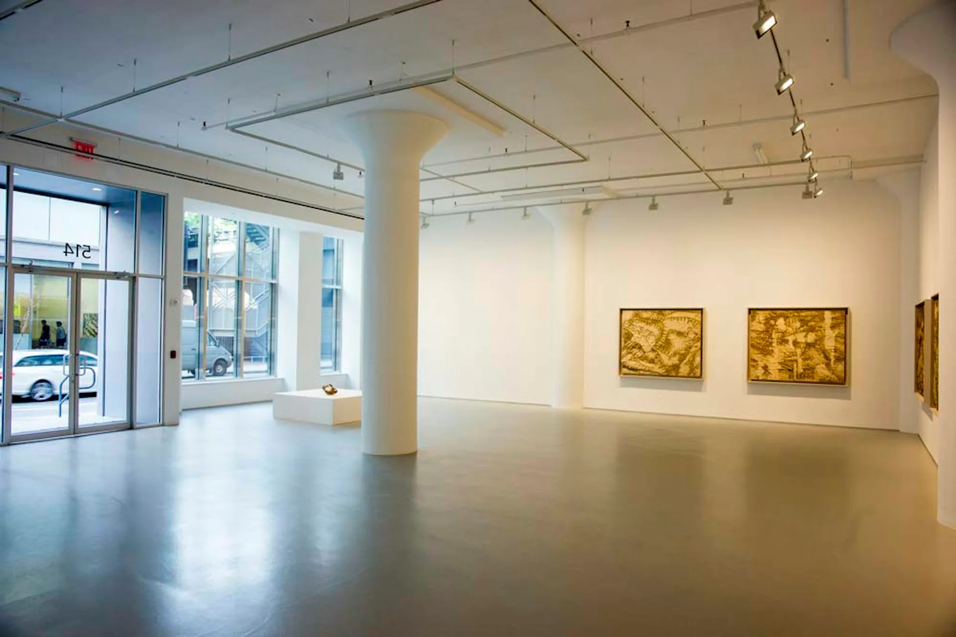 Minimalist gallery space with polished concrete floors, white walls, and track lighting displaying gold-toned artwork by Design AIDD Architecture, DPC.