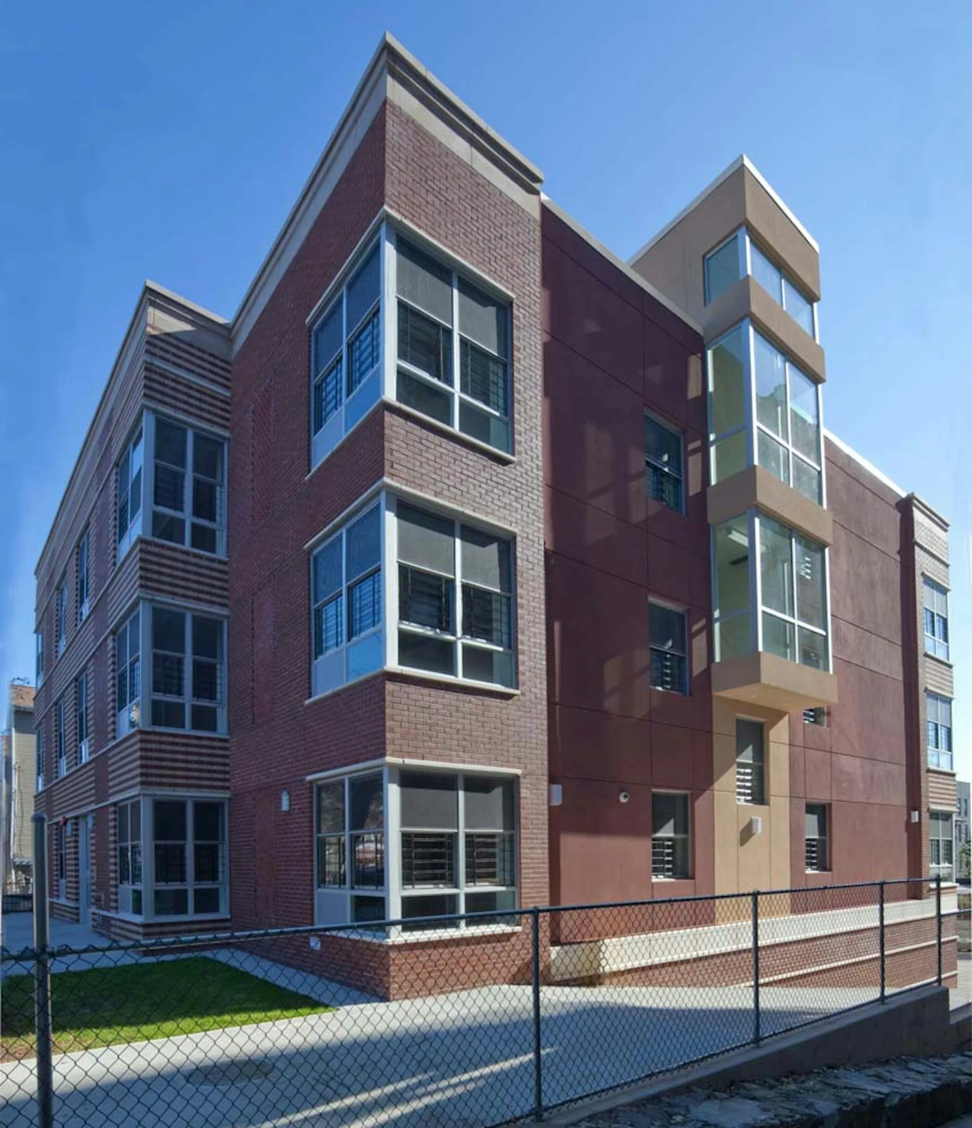 Contemporary multi-story brick residential building with protruding window bays, tan and burgundy facade, and steel mesh fencing by Design AIDD Architecture, DPC.