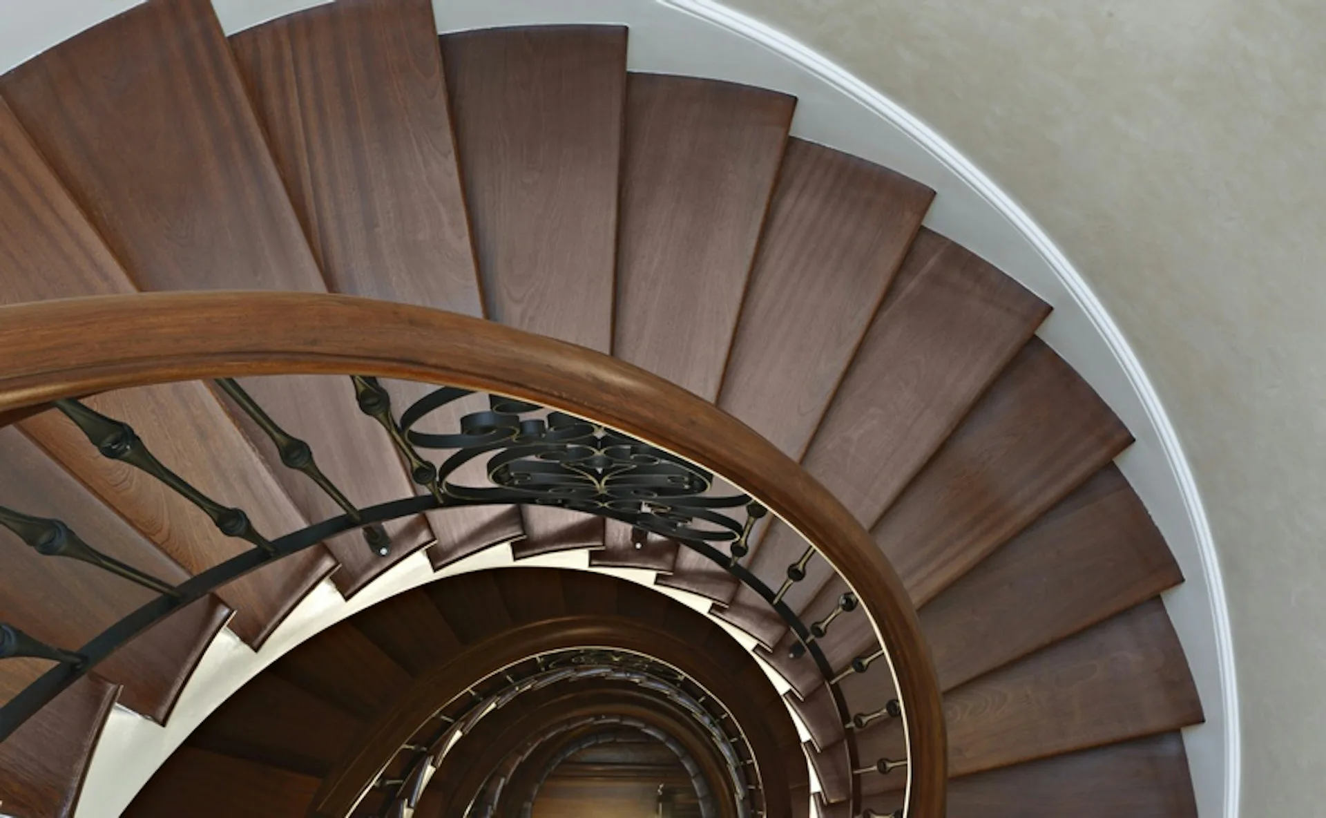 Spiral staircase with wooden treads and white curved walls, featuring metal railings, photographed from above by Design AIDD Architecture, DPC.