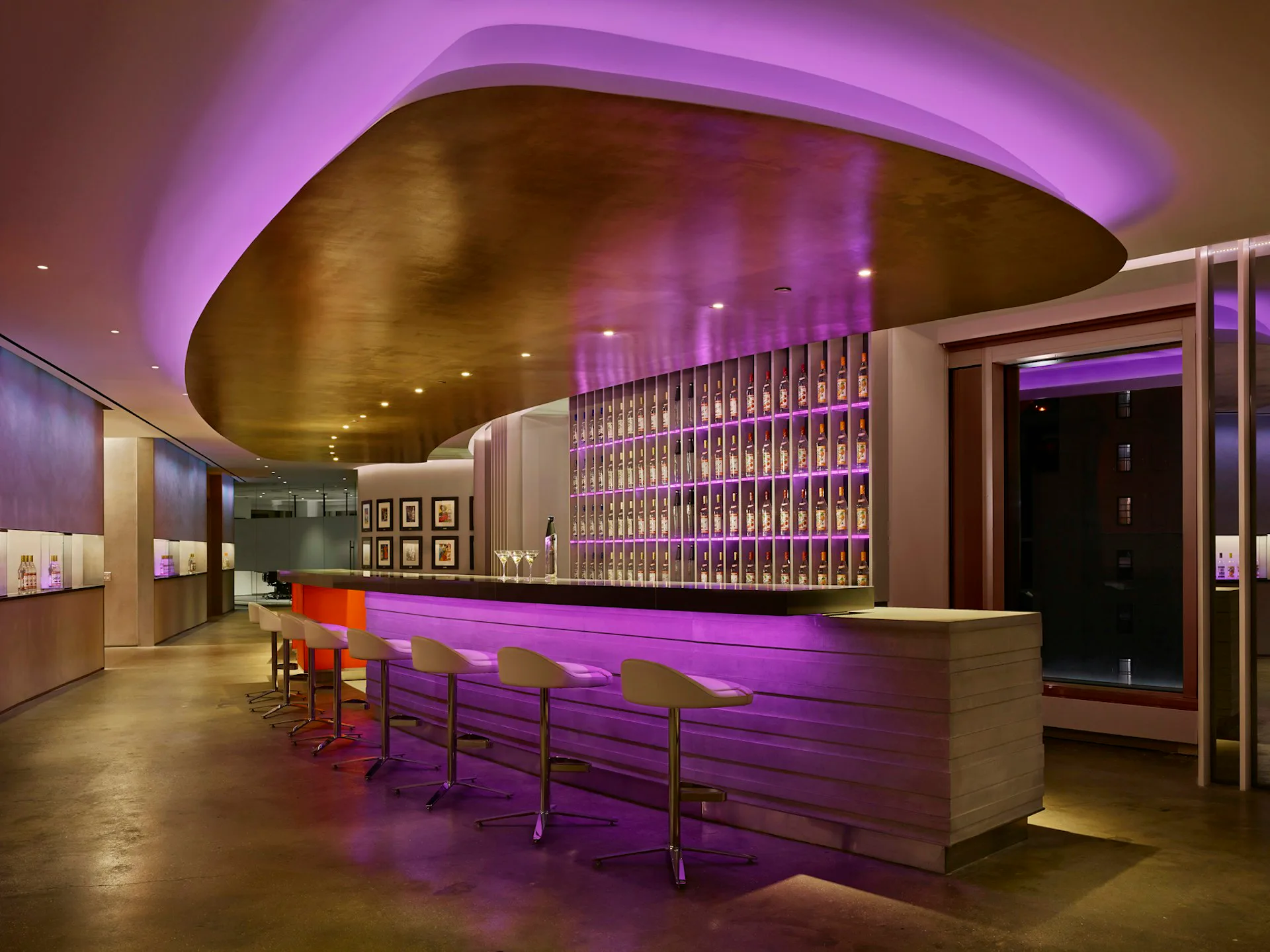 Modern bar interior with curved bronze ceiling, purple ambient lighting, illuminated bottle wall, and purple-upholstered seating by Design Republic.