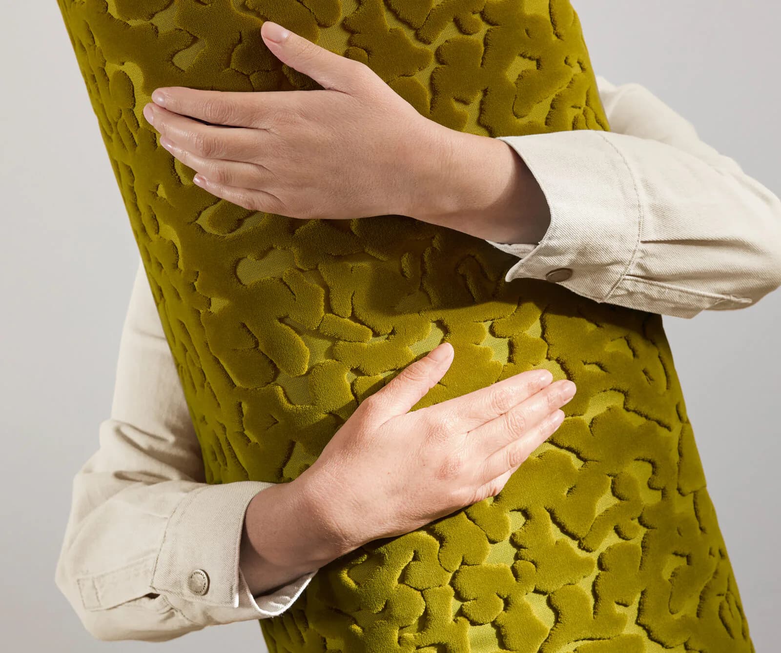 Hands embrace a textured chartreuse fabric with embossed geometric patterns, showcasing tactile material design by Designtex.