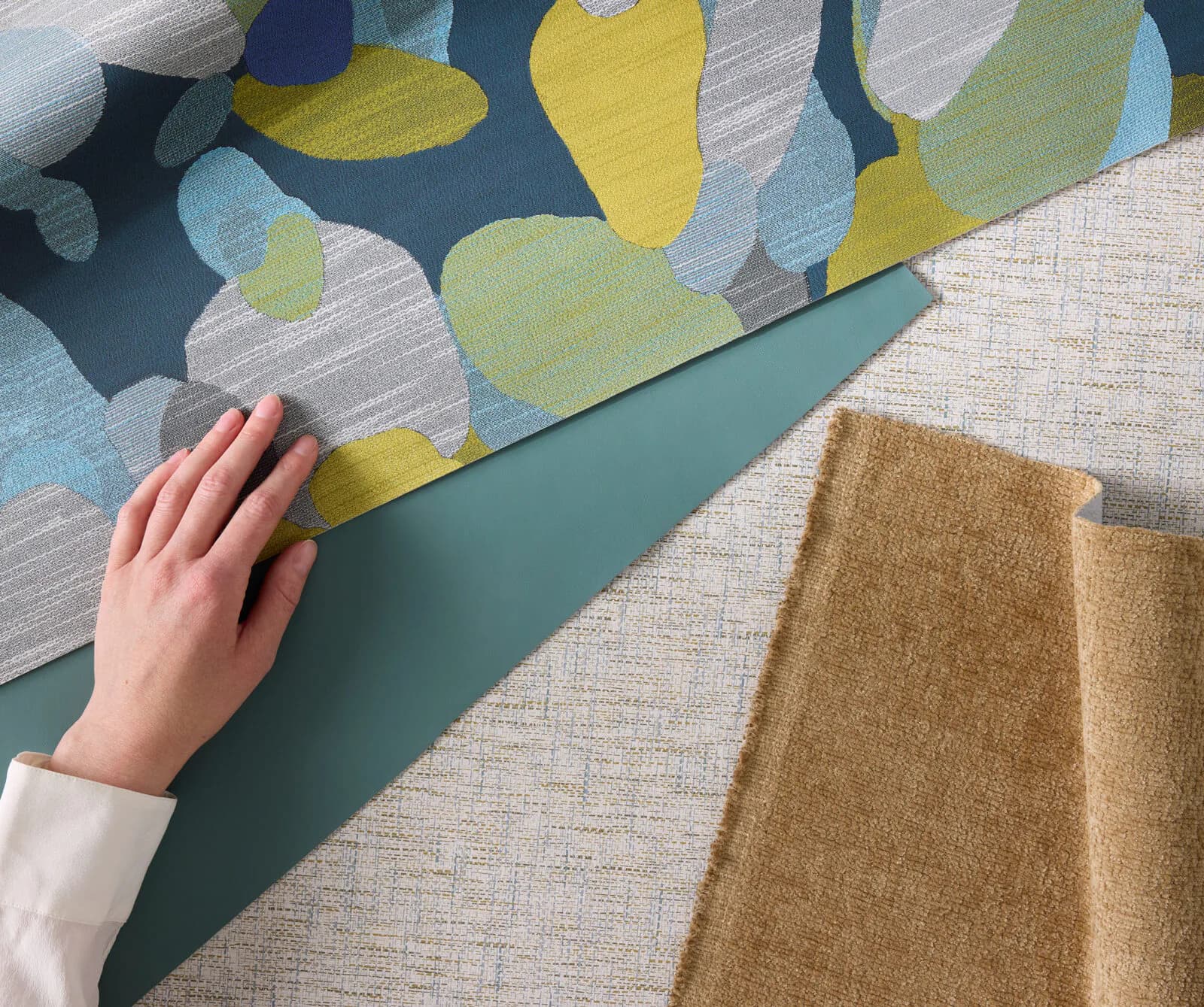 Fabric and material samples displayed together featuring a patterned textile with yellow and blue geometric shapes, teal accent piece, and woven neutral-toned fabrics by Designtex.