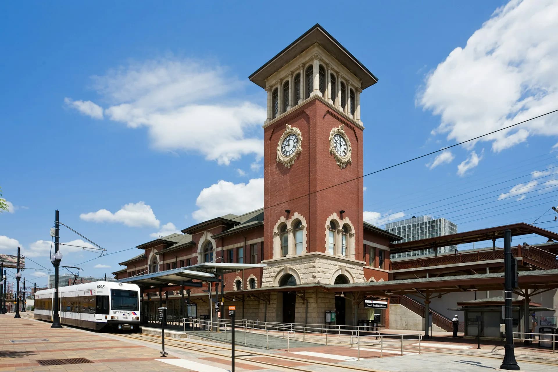 Brick clock tower transit station with arched windows and classical detailing, featuring modern steel canopies and plaza designed by di Domenico + Partners, LLP.