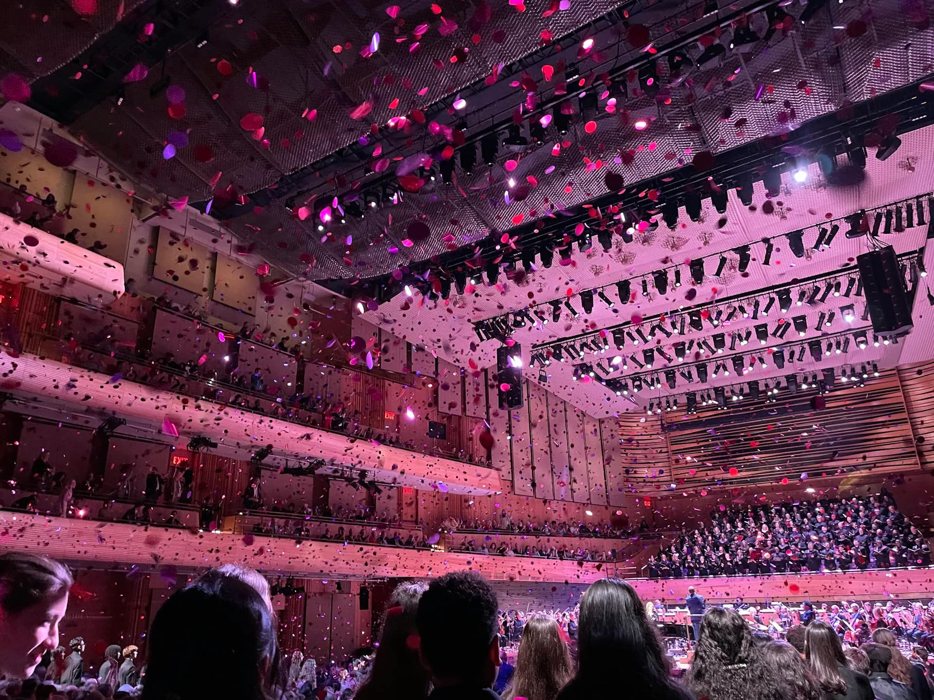 Grand concert hall interior bathed in pink and purple lighting, with multiple balcony levels filled with audiences and ornate architectural detailing by Diamond Schmitt.