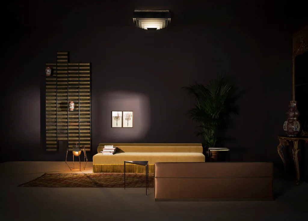 Dark luxury showroom with golden ochre upholstered seating, slatted wood wall panel, potted plant, and ambient lighting by Dimoremilano.