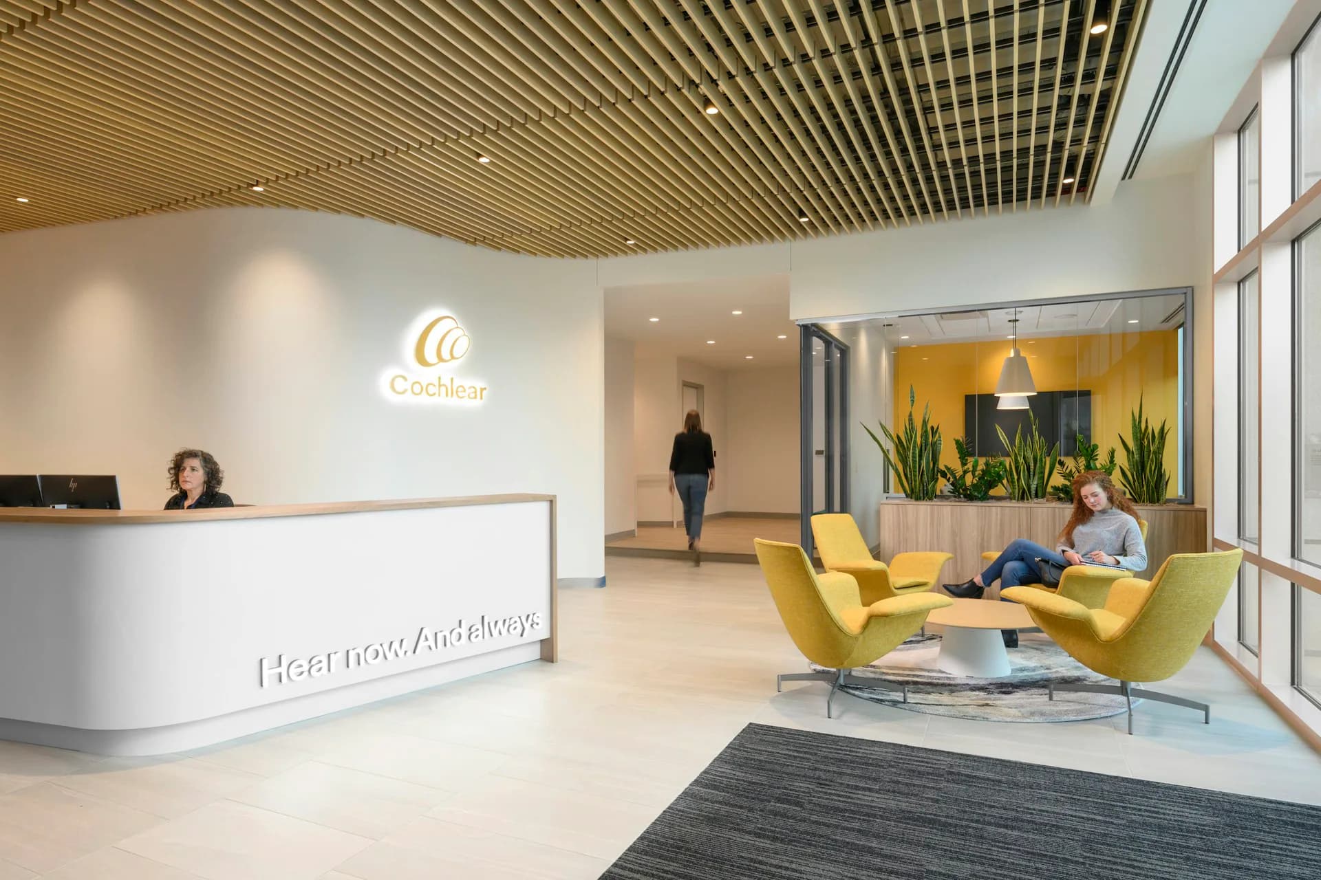 Modern office reception area with curved white desk, yellow seating, natural wood ceiling, and large windows by DLR Group.