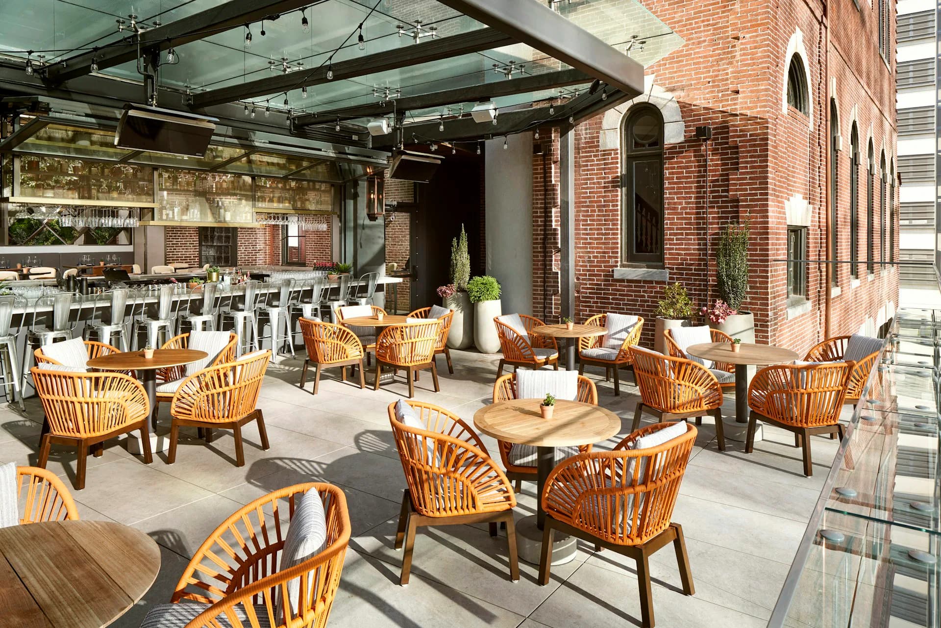 Rooftop terrace with brick facade, wooden chairs, concrete tables, and glass canopy structure by DLR Group.