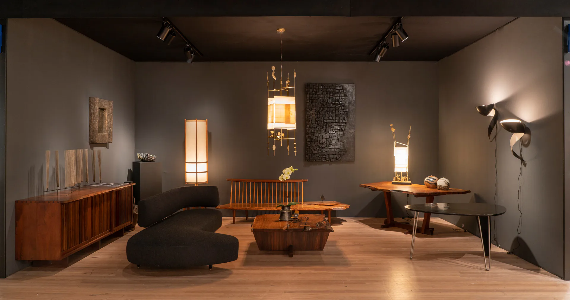 Modern interior showroom with warm wood flooring, sculptural black furniture, brass pendant lights, and minimalist shelving by Dobrinka Salzman Gallery.