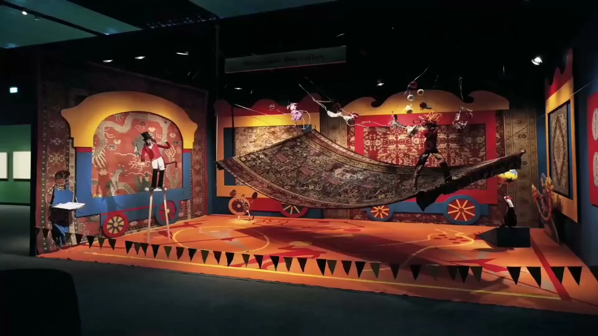 Vibrant museum exhibition display with orange wooden platform, red textile installations, and theatrical lighting creating an immersive cultural narrative by Doris Leslie Blau.