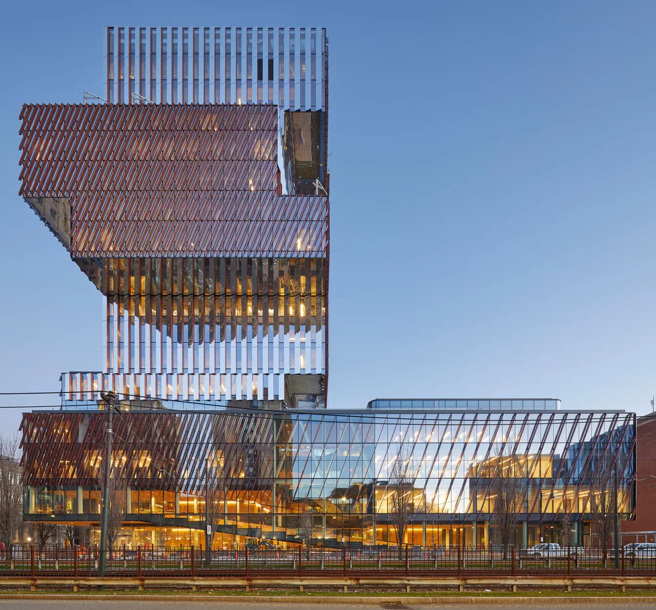 Stacked architectural tower with mixed materials including corrugated metal, vertical slats, and glass panels, illuminated at dusk by Dot Dash.