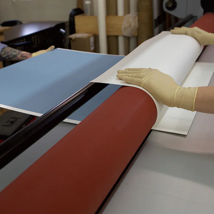 Hands in gloves carefully handling curved red and blue architectural materials during fabrication or installation work by Downing Frames.
