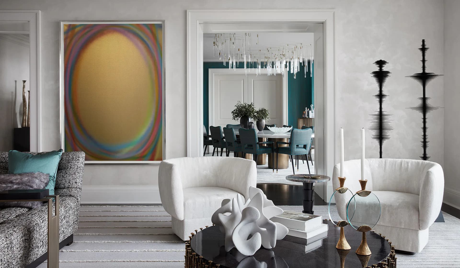 Modern living room with cream curved seating, white orchid arrangement, black candelabras, and colorful abstract artwork by /AND Design Studio.