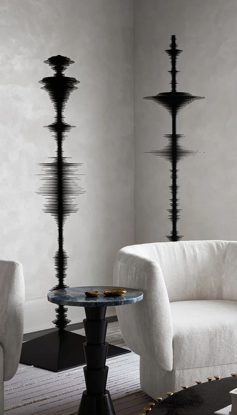 Modern interior with two sculptural black spiky column installations flanking a small round black side table between white curved armchairs by /AND Design Studio.