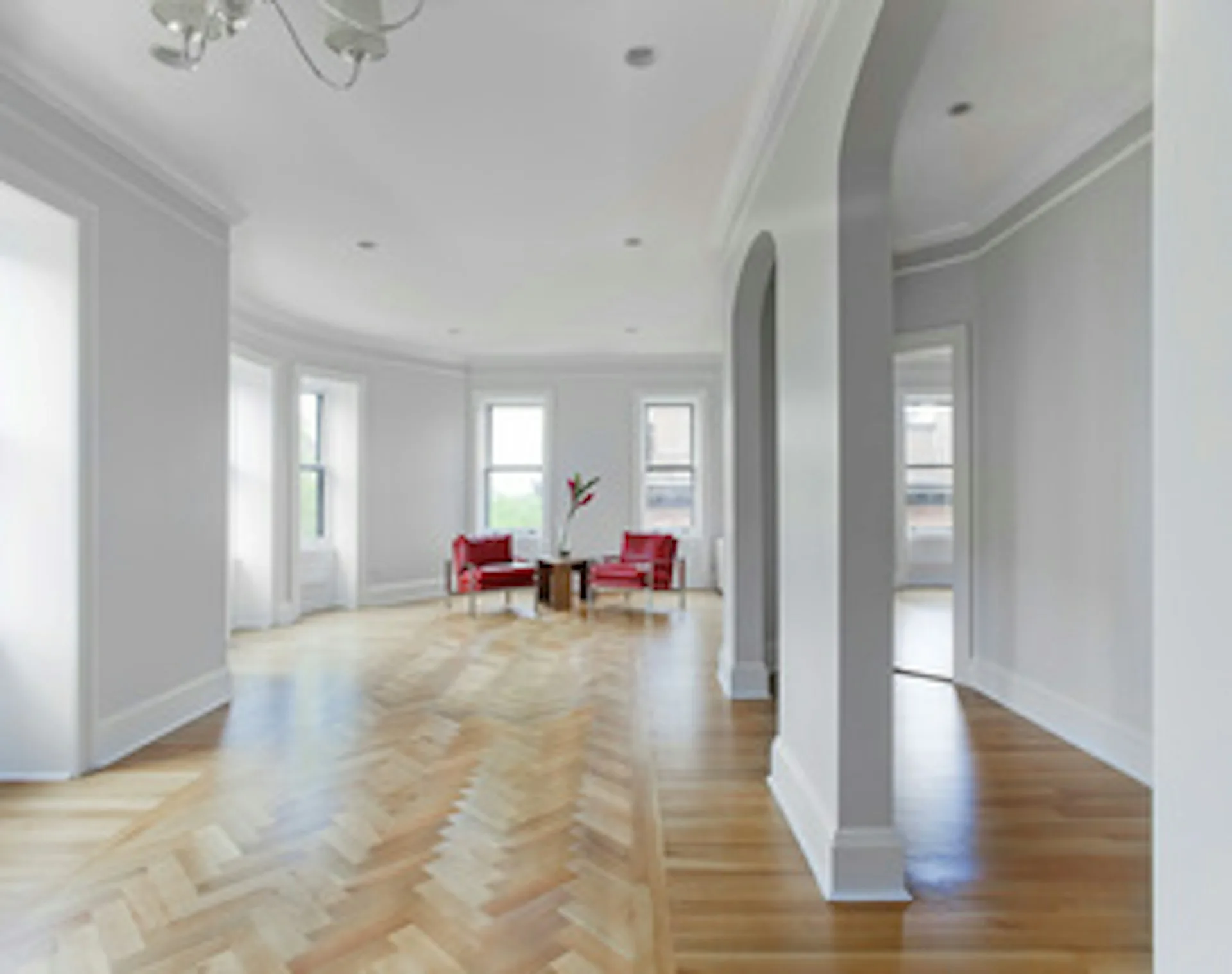 Spacious curved penthouse interior with herringbone wood flooring, white walls, tall windows, red accent chairs, and cylindrical structural columns by Ed Kopel, Architect, P.C.