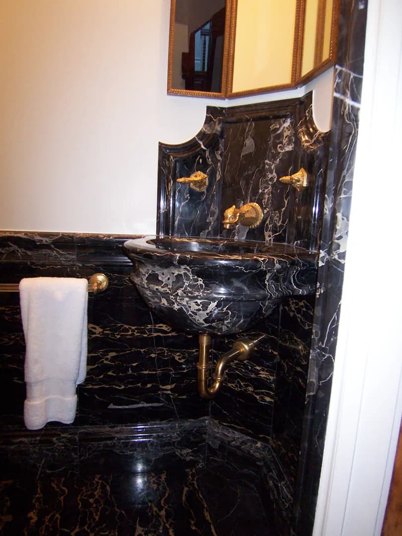 Luxurious bathroom vanity with black marble veining, gold brass fixtures, and decorative backsplash by Edward Dew Architect.