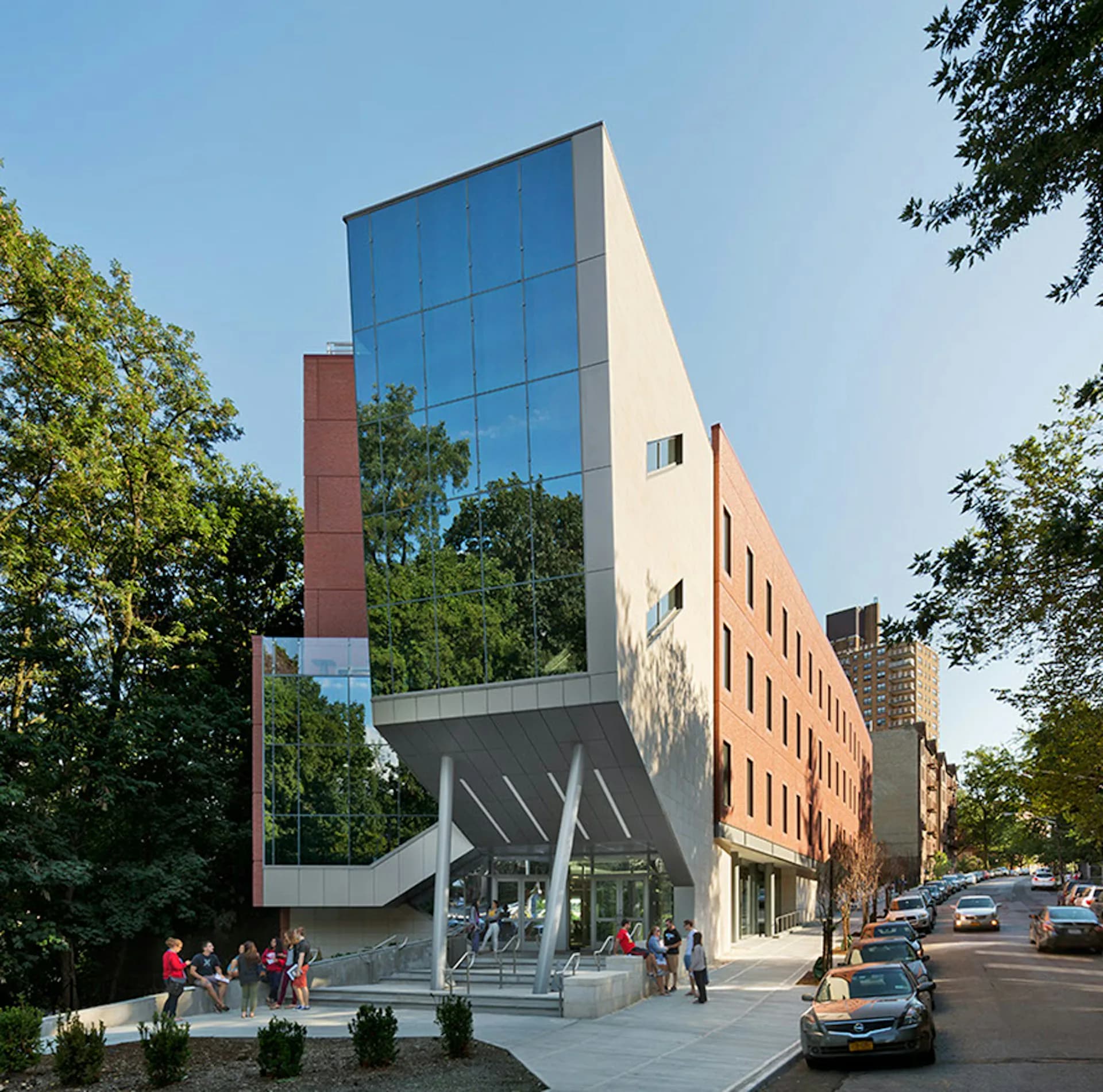 Modern mixed-use building with blue-glass upper facade and red-brick lower section, featuring dramatic angular canopy entrance and street-level retail by Edward I. Mills & Associates.