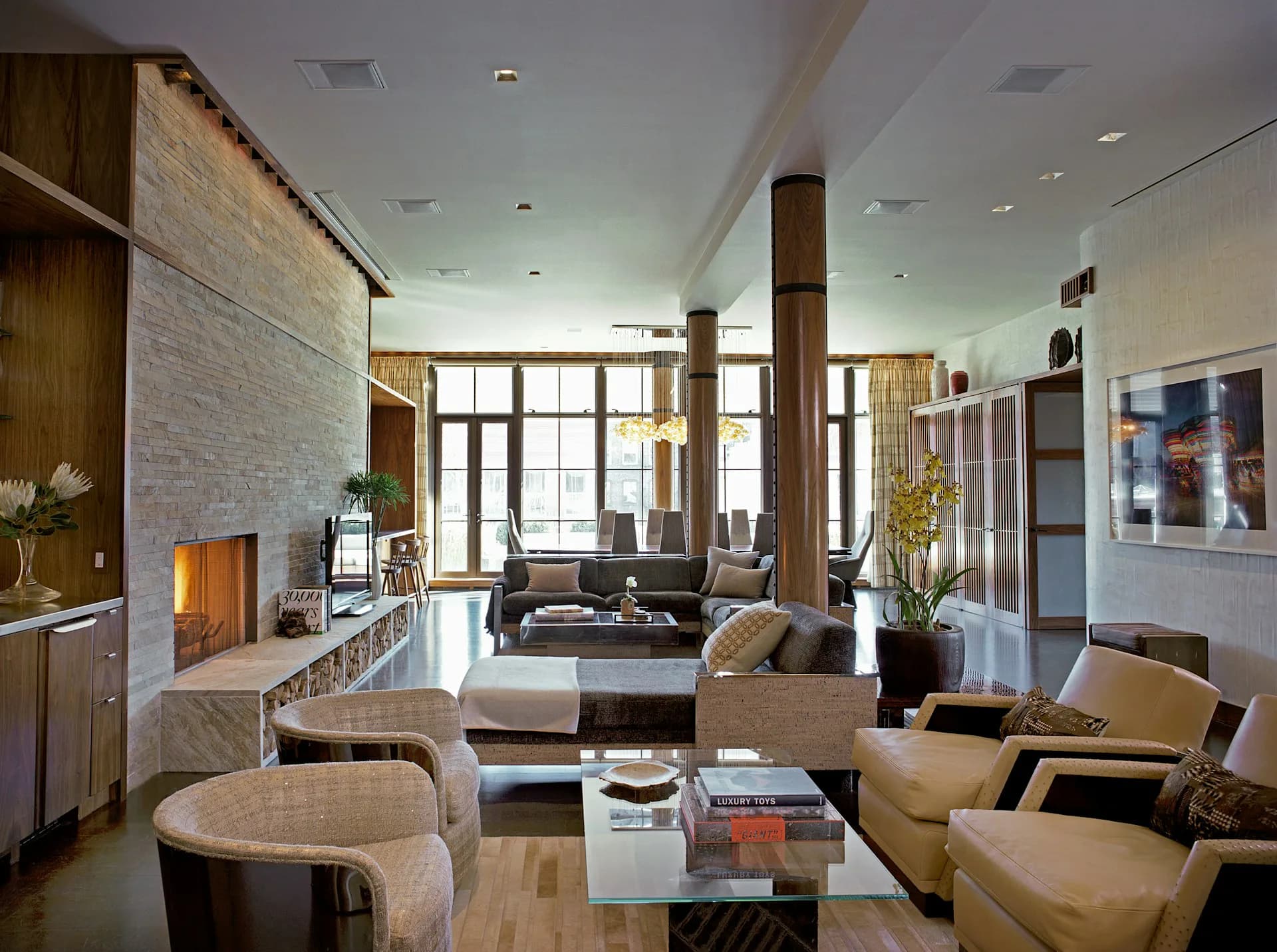 Modern loft living room with exposed brick, steel columns, and floor-to-ceiling windows, featuring neutral furnishings and warm wood accents by Edward Siegel Architect.