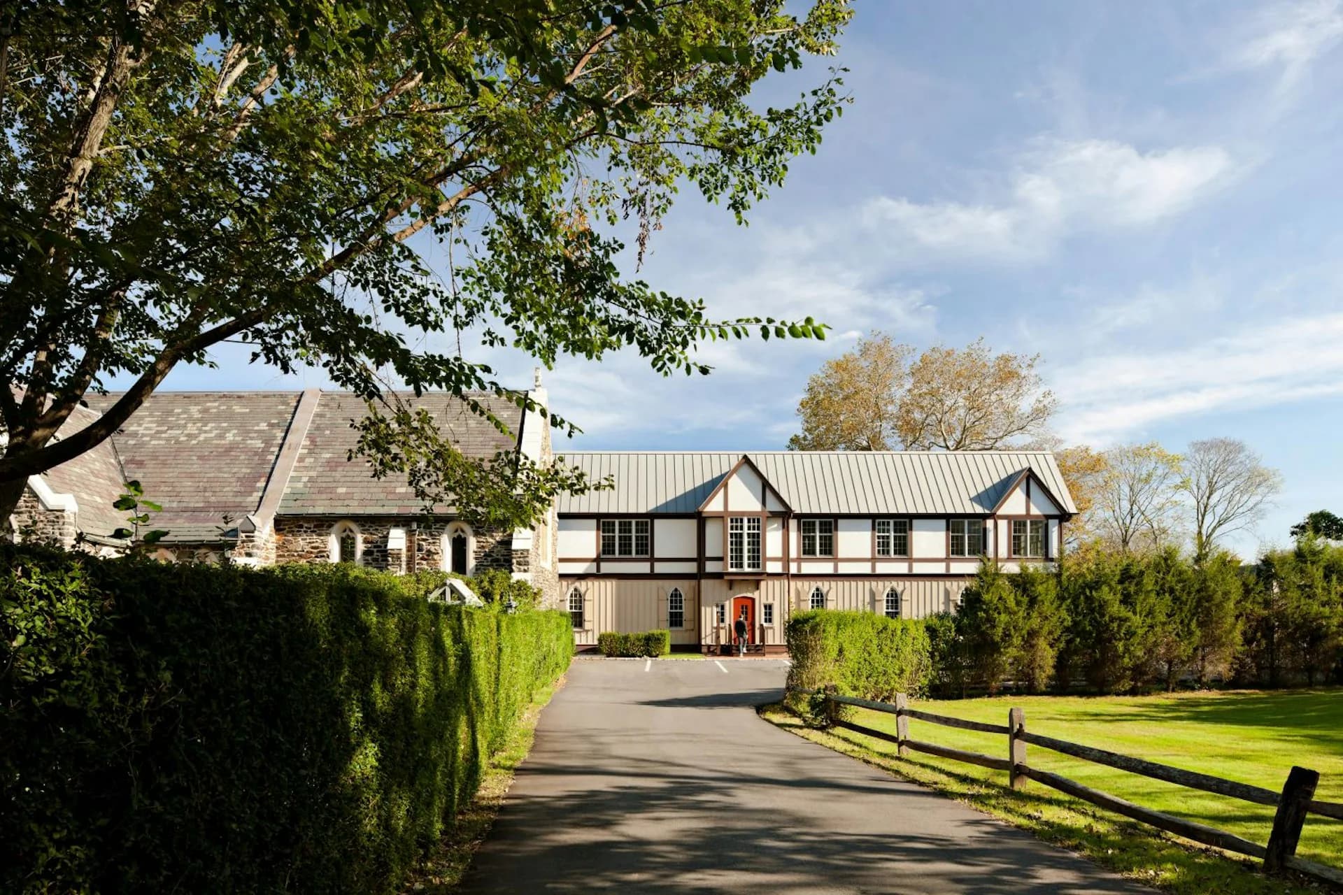 Modern farmhouse with black and white exterior, metal roof, and manicured grounds framed by trees and fencing, by Edward Siegel Architect.