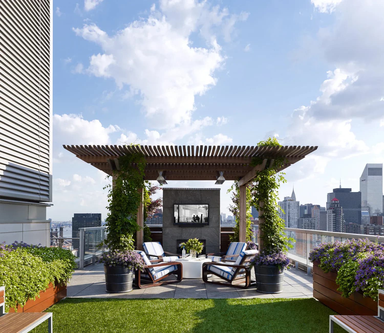 Modern rooftop terrace with pergola, planted in lush greenery and flowers, featuring lounge seating overlooking a city skyline by Edward Siegel Architect.