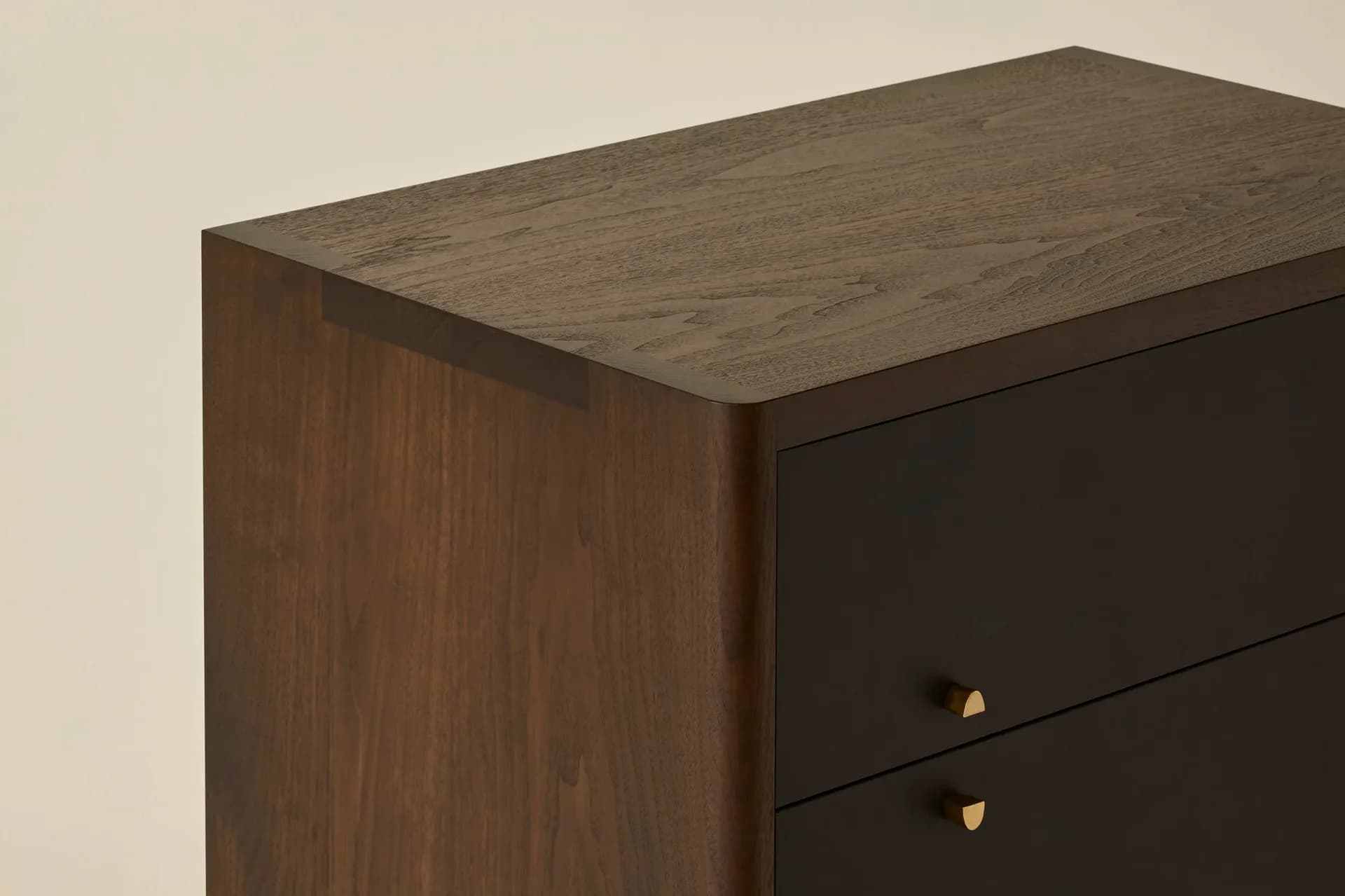 Dark wood dresser with two drawers and brass hardware, photographed against a neutral beige wall, showcasing minimalist furniture design by Egg Collective.