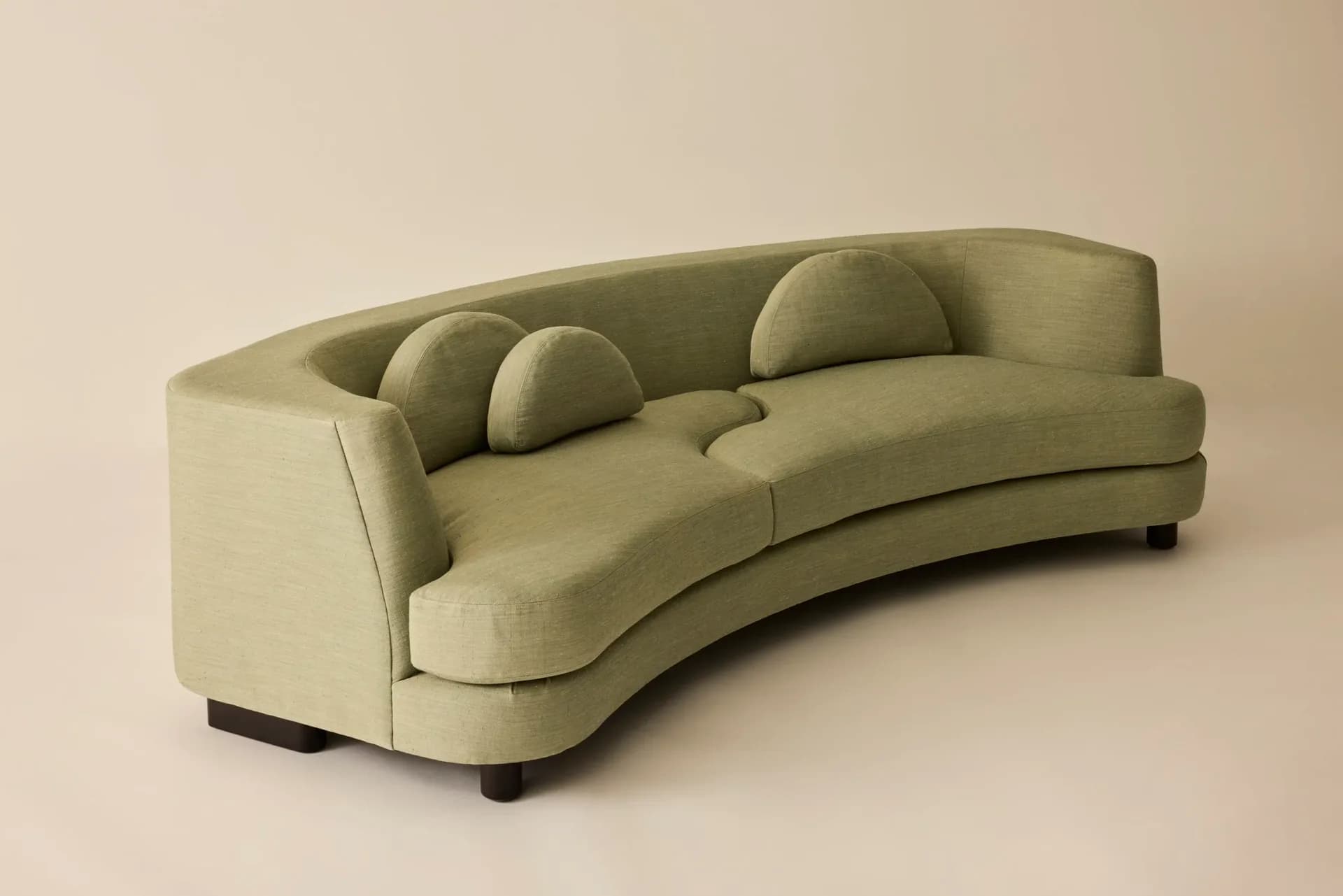 Curved sage green upholstered sofa with cylindrical throw pillows and dark wooden legs, rendered with soft studio lighting by Egg Collective.
