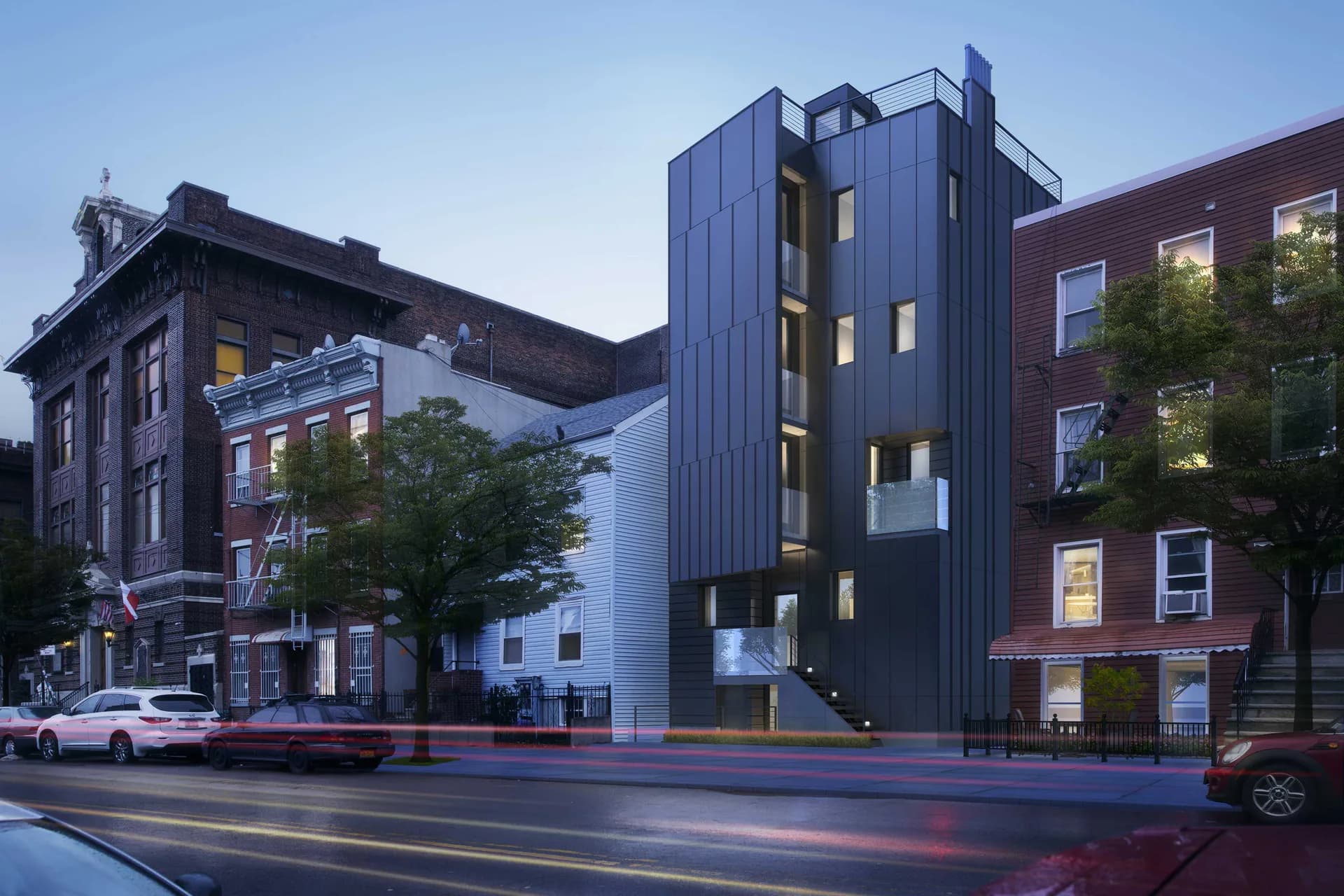 Dark blue-black contemporary residential building with illuminated window openings, featuring a sculptural form integrated between historic brick structures on an urban street corner by Elemental Architecture LLC.