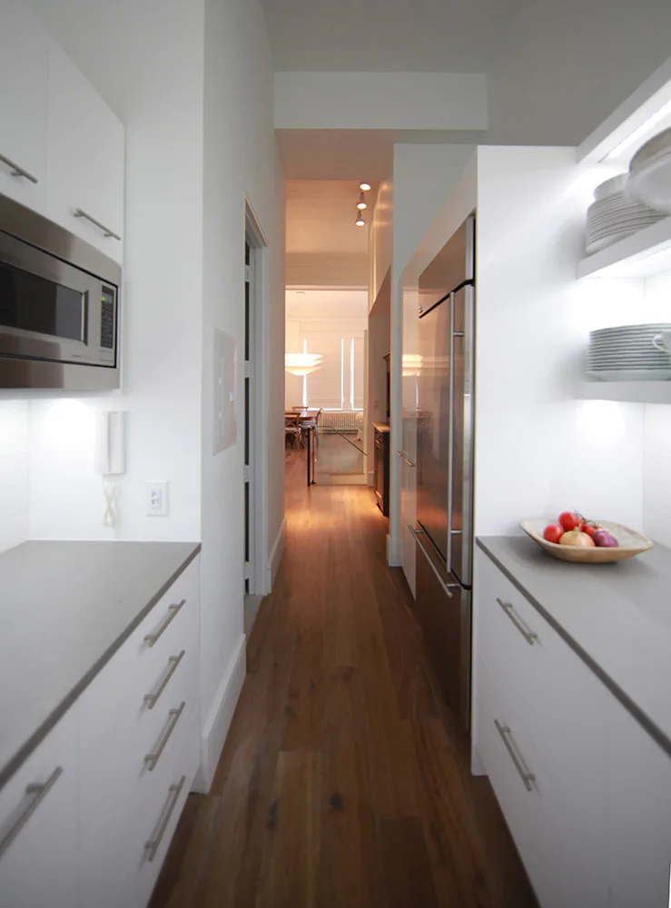Modern galley kitchen with white cabinetry, stainless steel appliances, and dark wood flooring, designed by Elemental Architecture LLC.