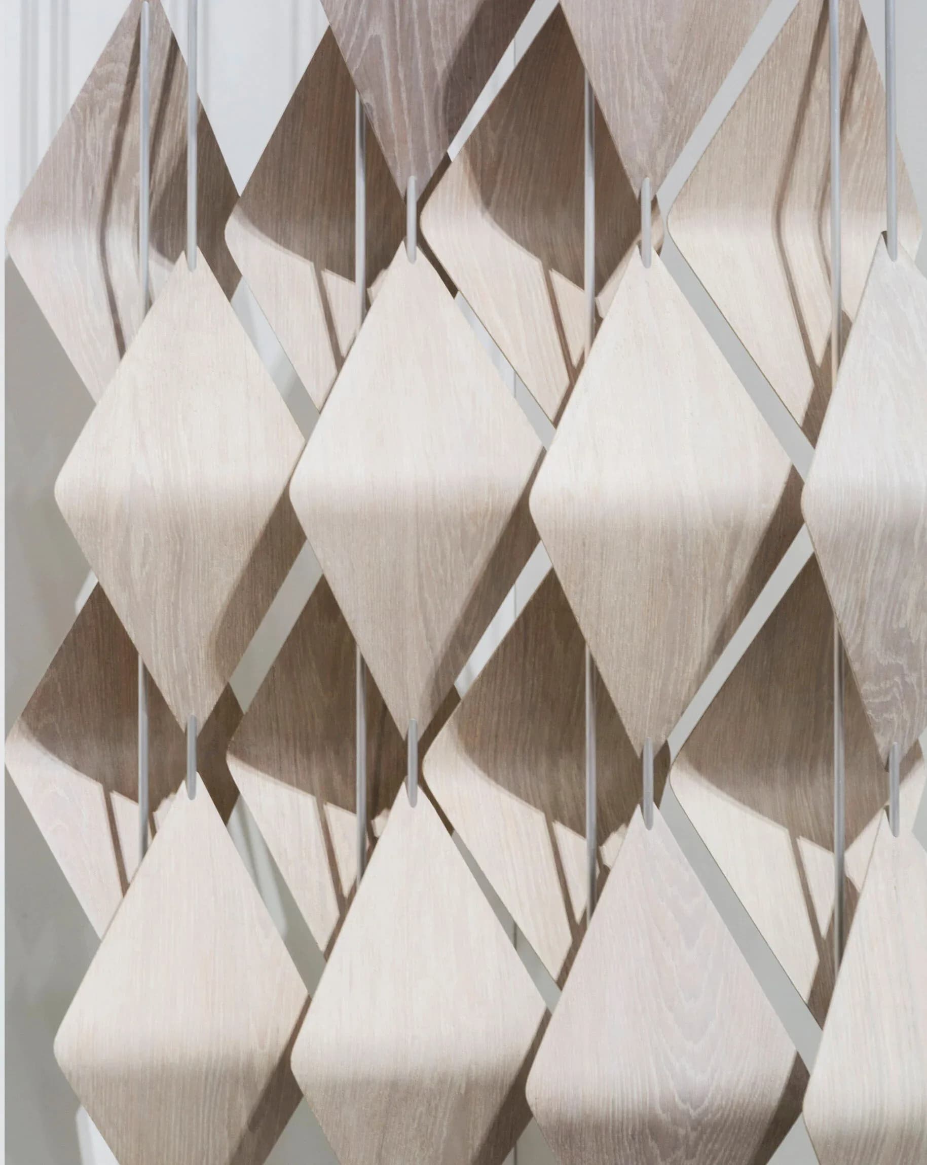 Sculptural wall installation featuring layered wooden diamond-shaped panels in cream and natural wood tones creating dimensional shadow play by Elish Warlop Design Studio.