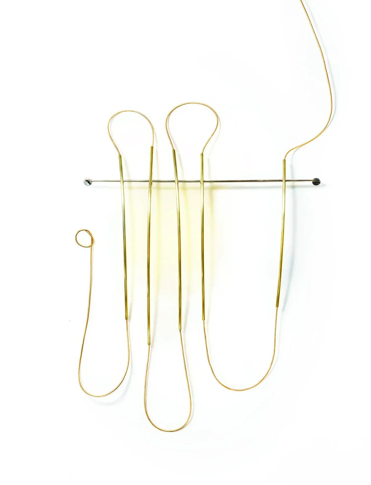 Golden brass wire sculpture installation featuring looped forms mounted on a horizontal rod, creating an abstract three-dimensional composition by Elish Warlop Design Studio.