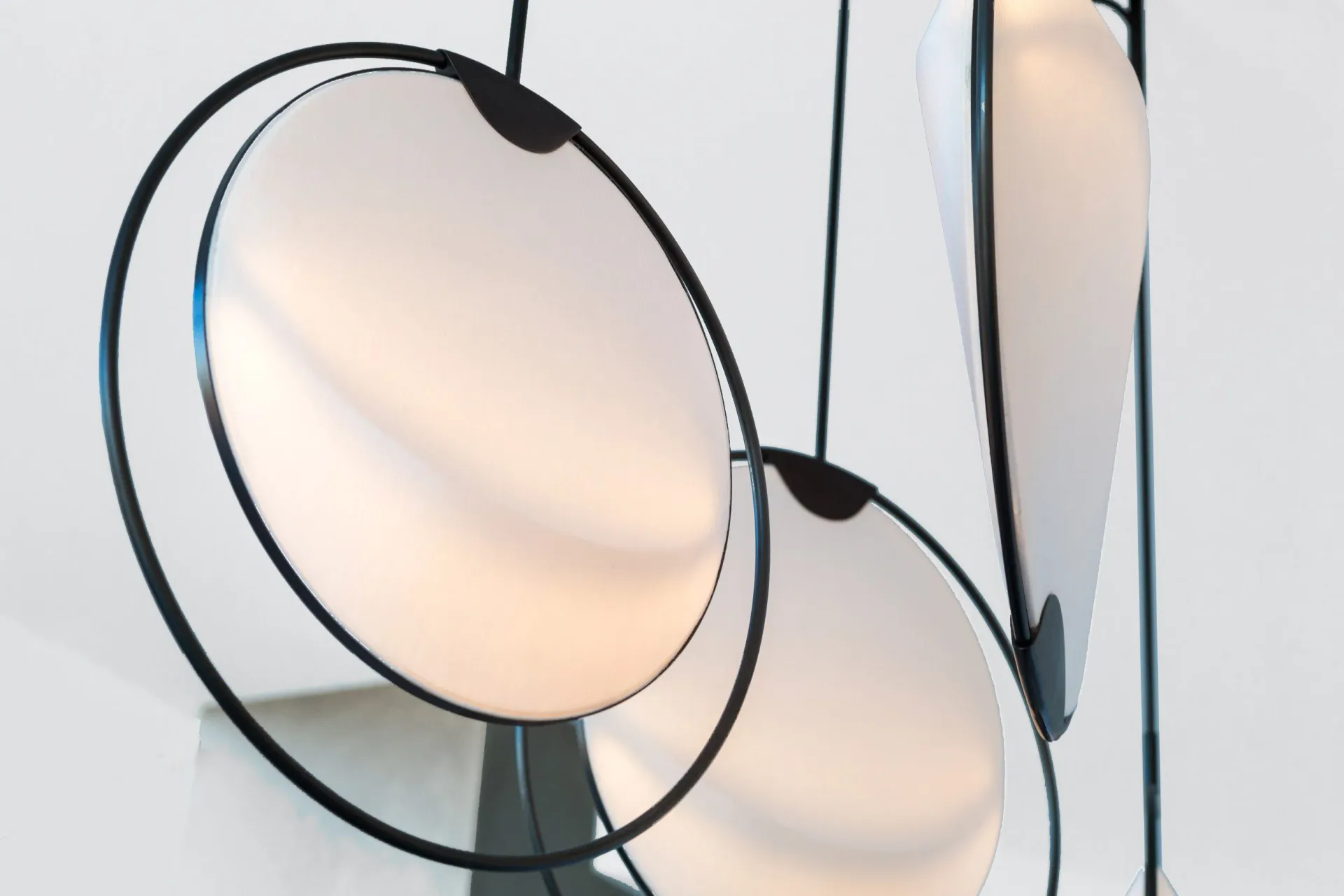 Sculptural pendant lighting installation with circular frosted glass diffusers suspended by dark metal frames against a neutral backdrop by Elish Warlop Design Studio.
