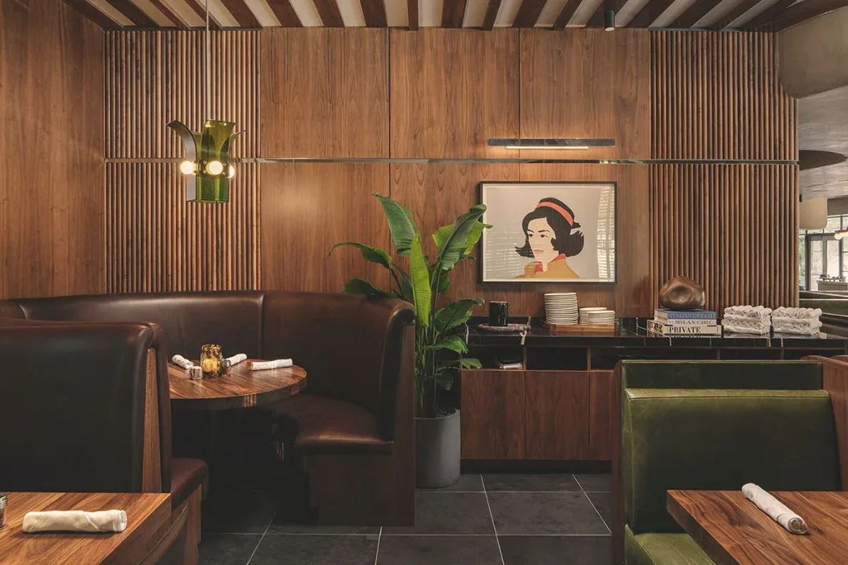 Mid-century modern restaurant interior with walnut wood paneling, leather banquettes, brass lighting, and warm ambient lighting by Ember Studio.