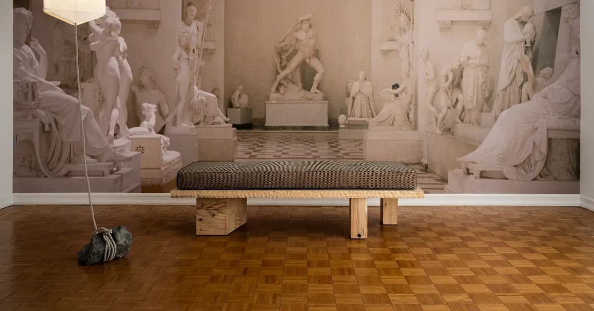 Neoclassical gallery interior with plaster casts and sculptures lining cream walls, polished wood herringbone floor, and minimalist wooden pedestals by Emma Scully Gallery.