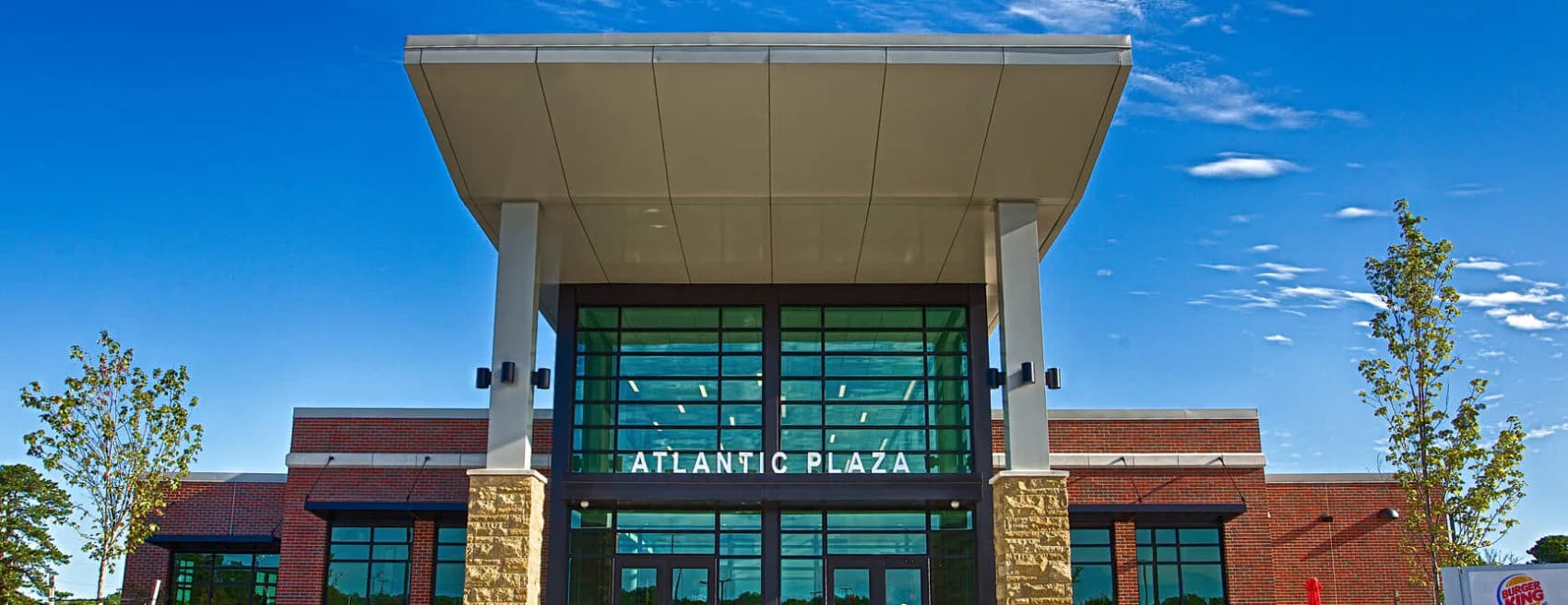 Atlantic Plaza building exterior featuring brick and stone facades with green-tinted glass storefront entrance under a blue sky, designed by ENV - New Jersey.