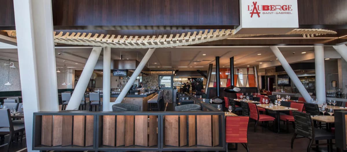 Modern restaurant interior featuring a dark wood ceiling, white structural columns, and a bronze-toned bar counter with red dining seating visible in the background by ENV - New Jersey.