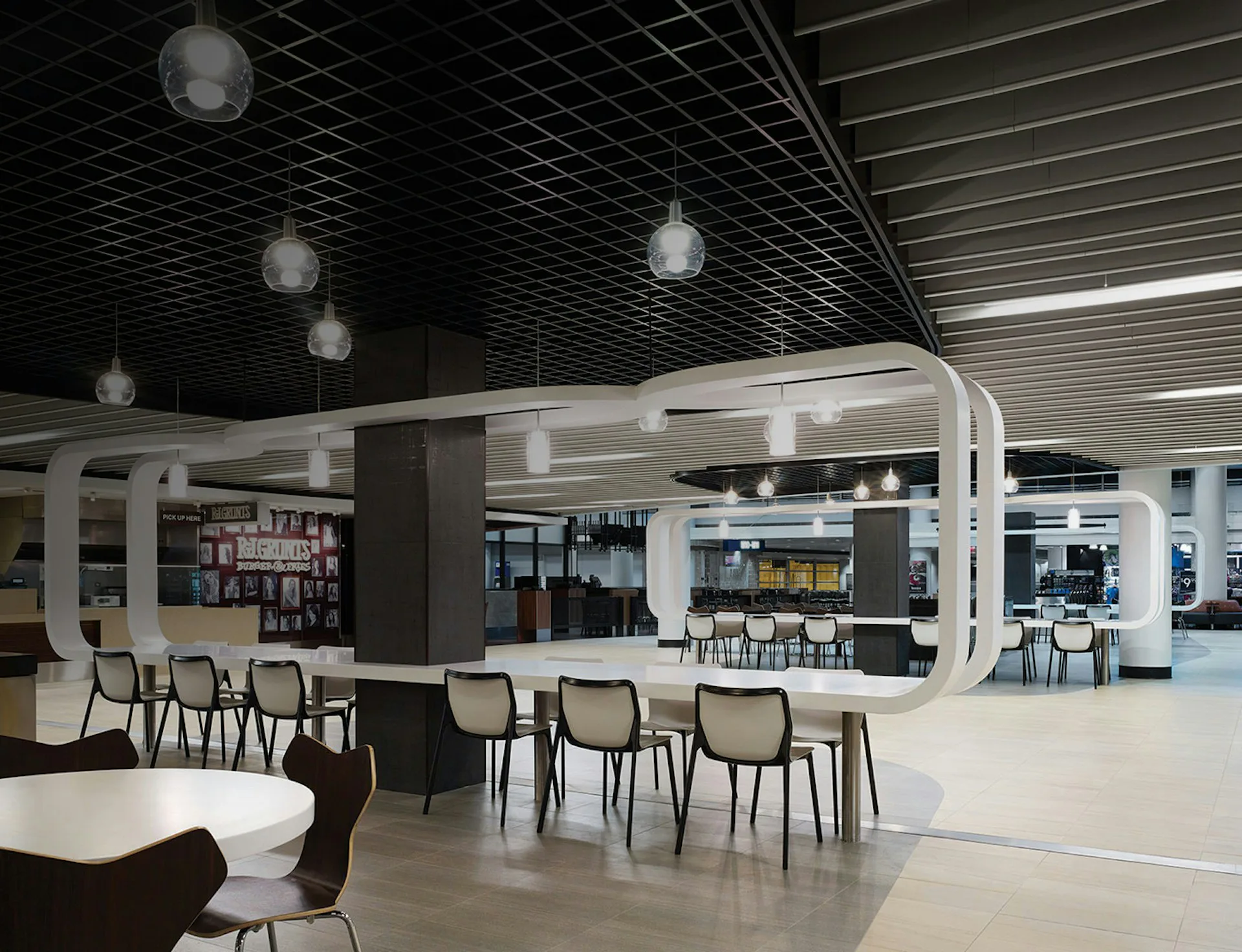 Modern cafeteria with curved white architectural elements, pendant lighting, gray seating, and polished concrete floors by Epstein Global.