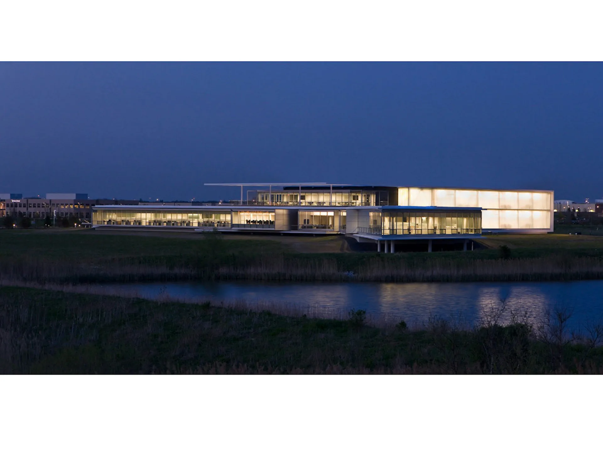 Illuminated contemporary waterfront building with glass and stone facades reflected in still water at dusk, designed by Epstein Global.