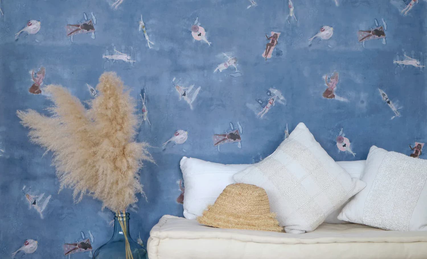 Blue wallpapered bedroom wall with playful animal motifs featuring a white bed with pillows, dried pampas grass, and straw hat by Eskayel.