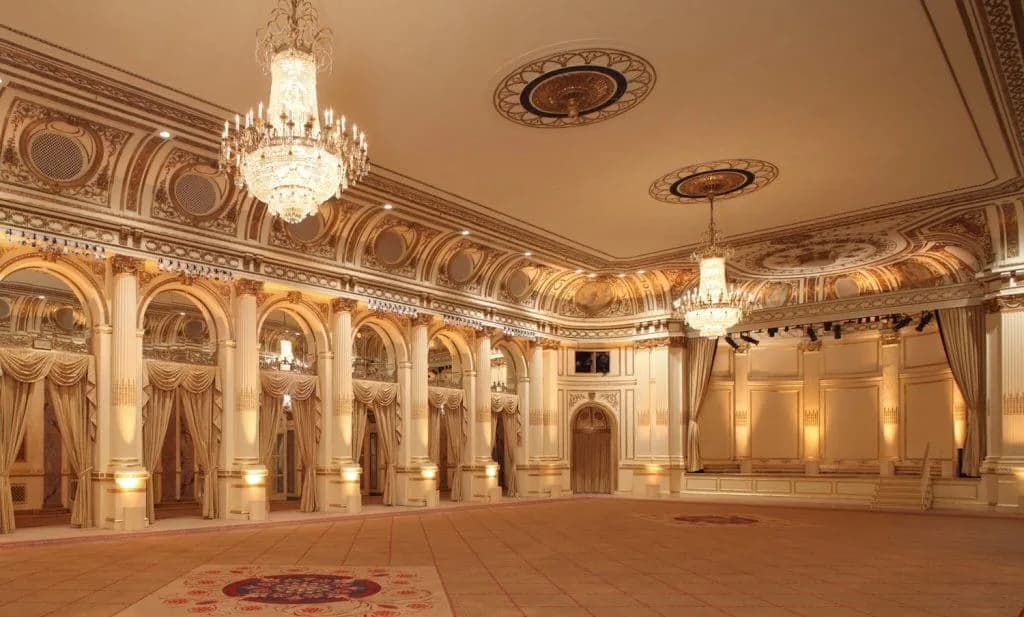 Grand ballroom with ornate classical plasterwork, arched alcoves, crystal chandeliers, and polished wood flooring by EverGreene Architectural Arts.