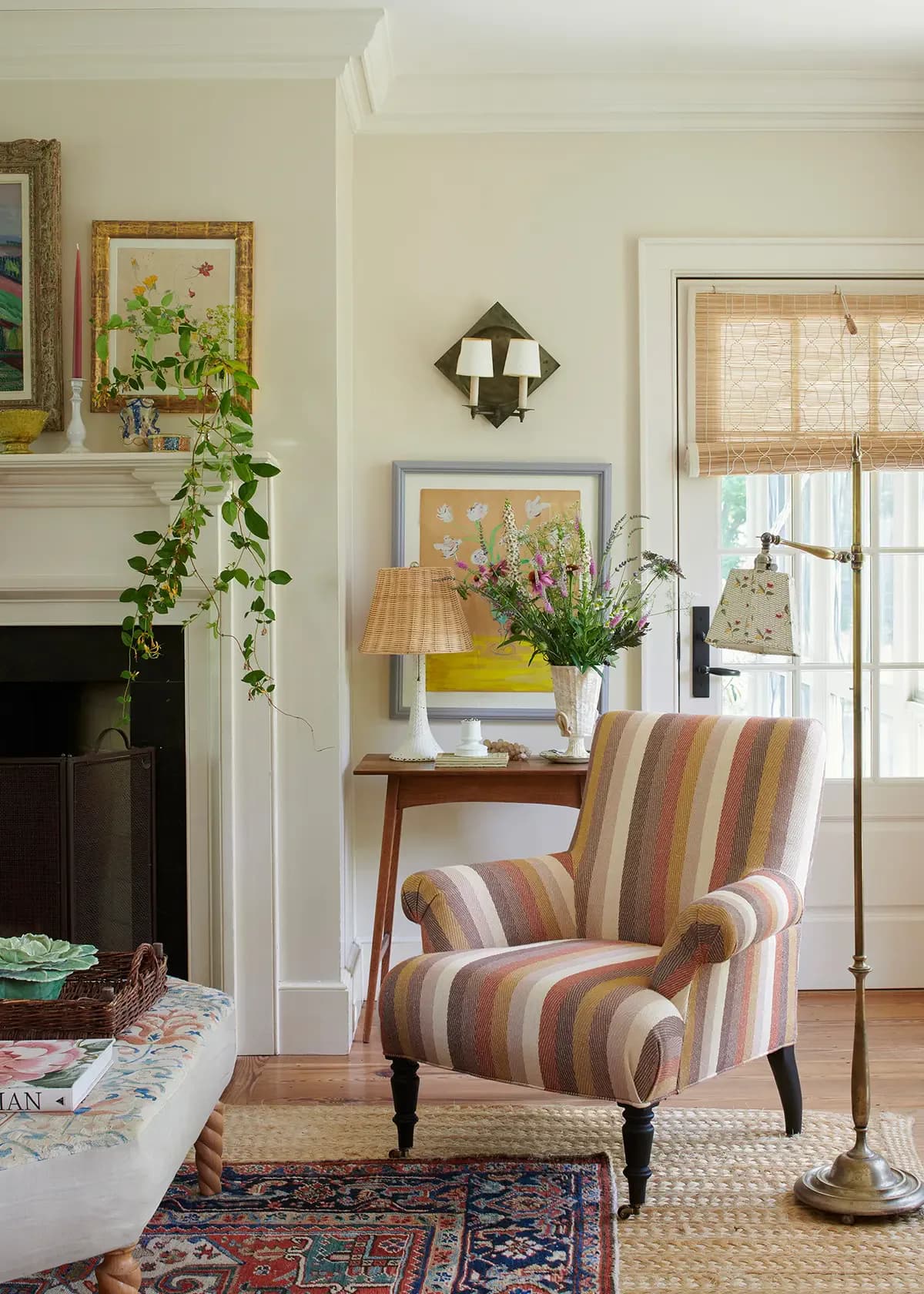 Cream living room with striped upholstered chair, wooden console table, fireplace, and vintage accessories arranged by F. Schumacher & Co.