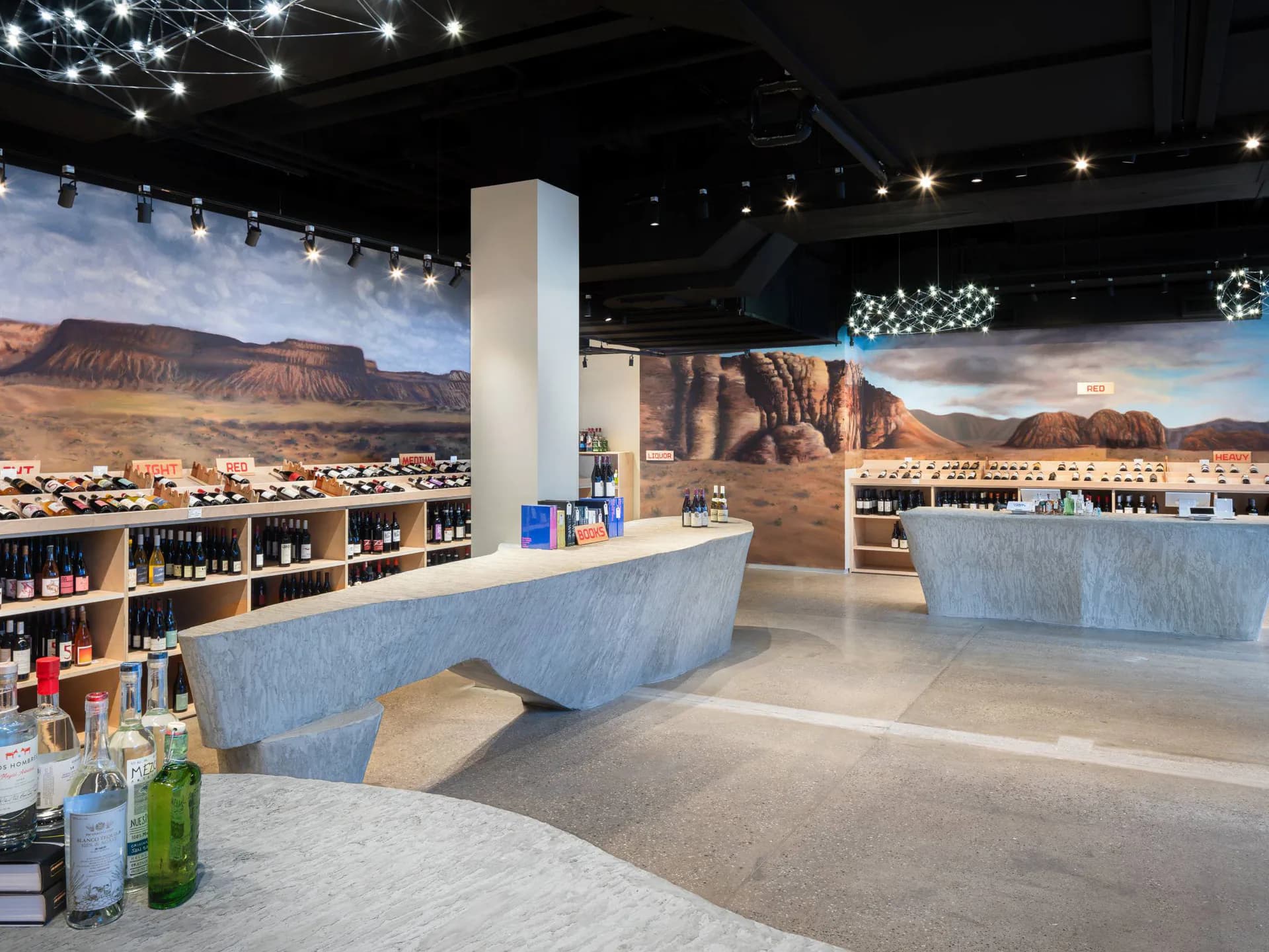 Modern tasting room with curved concrete counters, mountain backdrop murals, and wine displays by FAR Architecture.