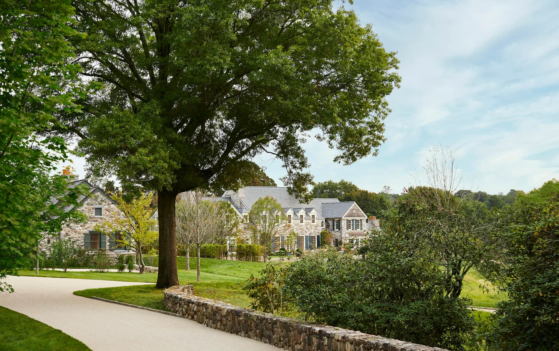 Expansive residential estate with stone facade and manicured grounds beneath a large mature oak tree, designed by Ferguson & Shamamian Architects.