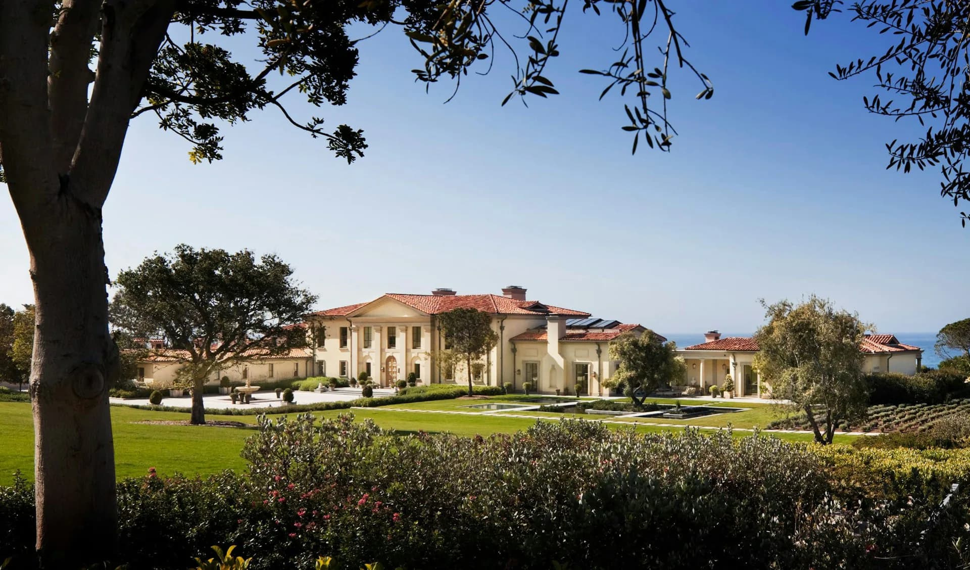 A Mediterranean-style villa with ochre stucco walls and terracotta roofing sits across manicured lawns and hedgerows, showcasing classical architectural proportions by Ferguson & Shamamian Architects.
