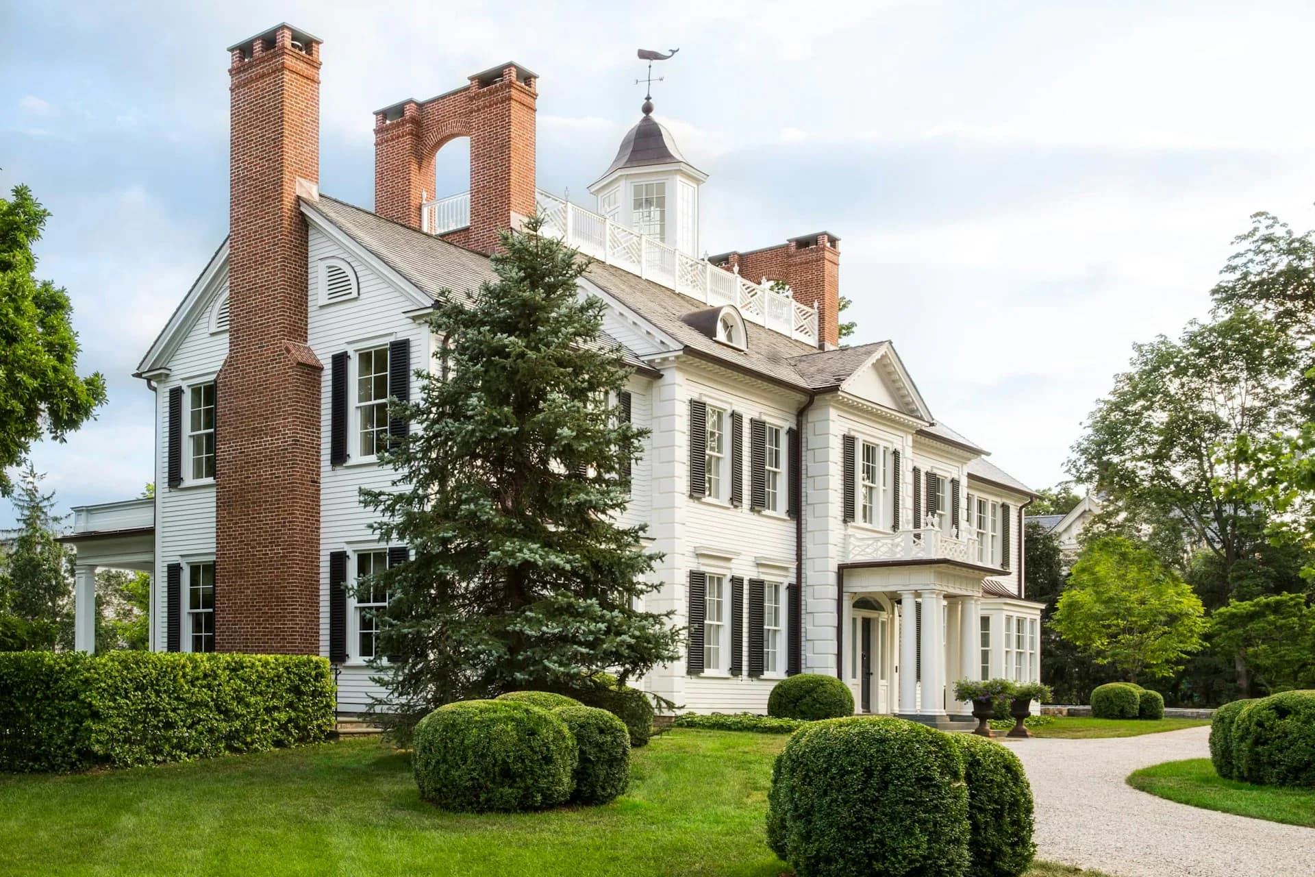 A stately colonial revival residence with brick and white painted wood exterior, featuring symmetrical façade, multiple chimneys, and manicured landscaping by Ferguson & Shamamian Architects.