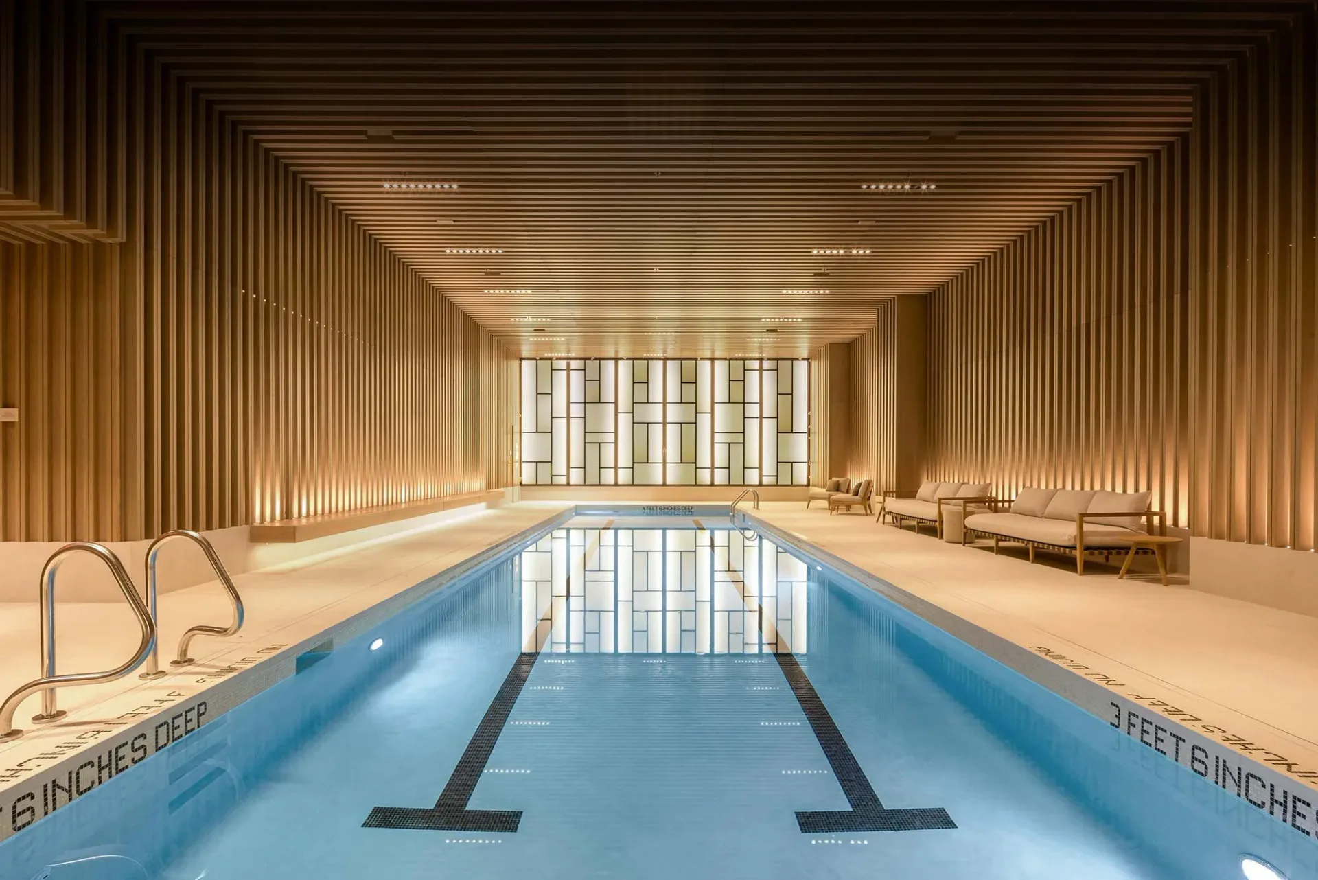Modern indoor swimming pool with warm wood-paneled walls, linear ceiling details, and lane markings, designed by Ferra Designs.