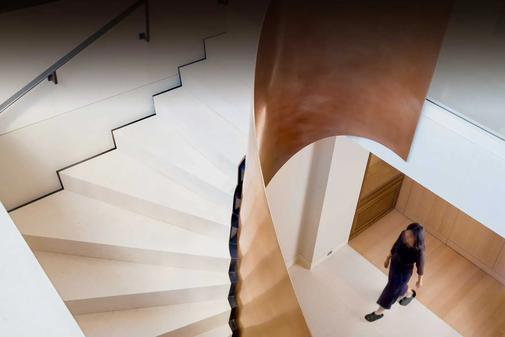 Minimalist wooden staircase with clean geometric lines and warm natural materials, photographed from above with a person on the landing, by Ferra Designs.